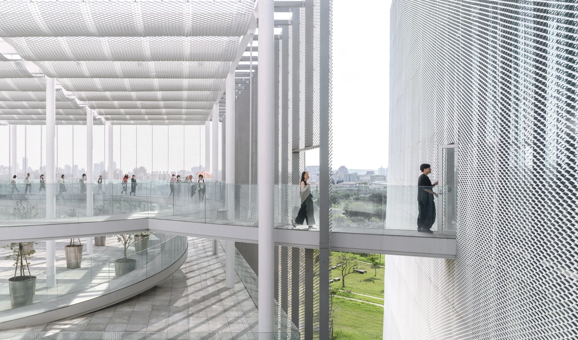 Taichung Art Museum by SANAA, photographed by Yi-Hsien Lee (YHLAA) — An upper terrace runs beneath a white steel grid pergola with a mesh soffit, glass balustrades and potted trees framing a long view over the park.