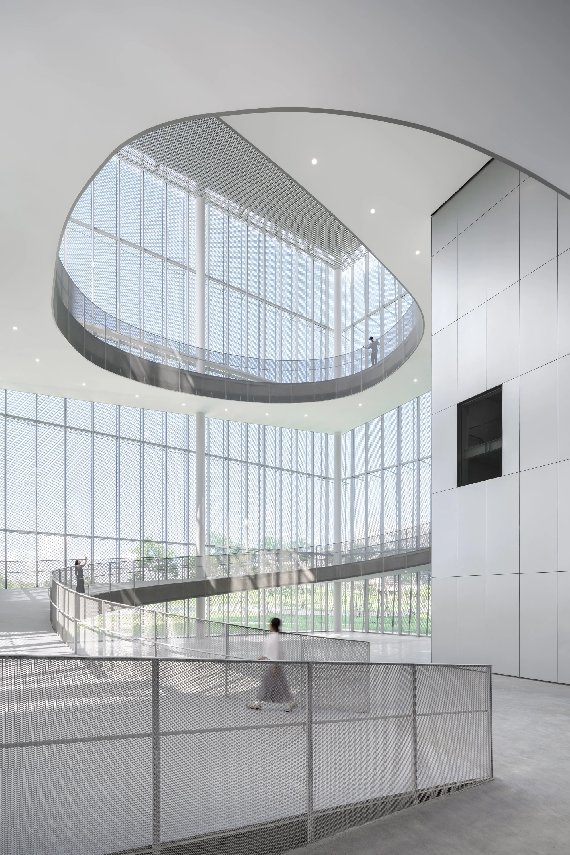 Taichung Art Museum by SANAA, photographed by Yi-Hsien Lee (YHLAA) — An oval is cut through the floor plate of the atrium, linking levels across a double-height void wrapped in mullioned glass and white mesh balustrades.