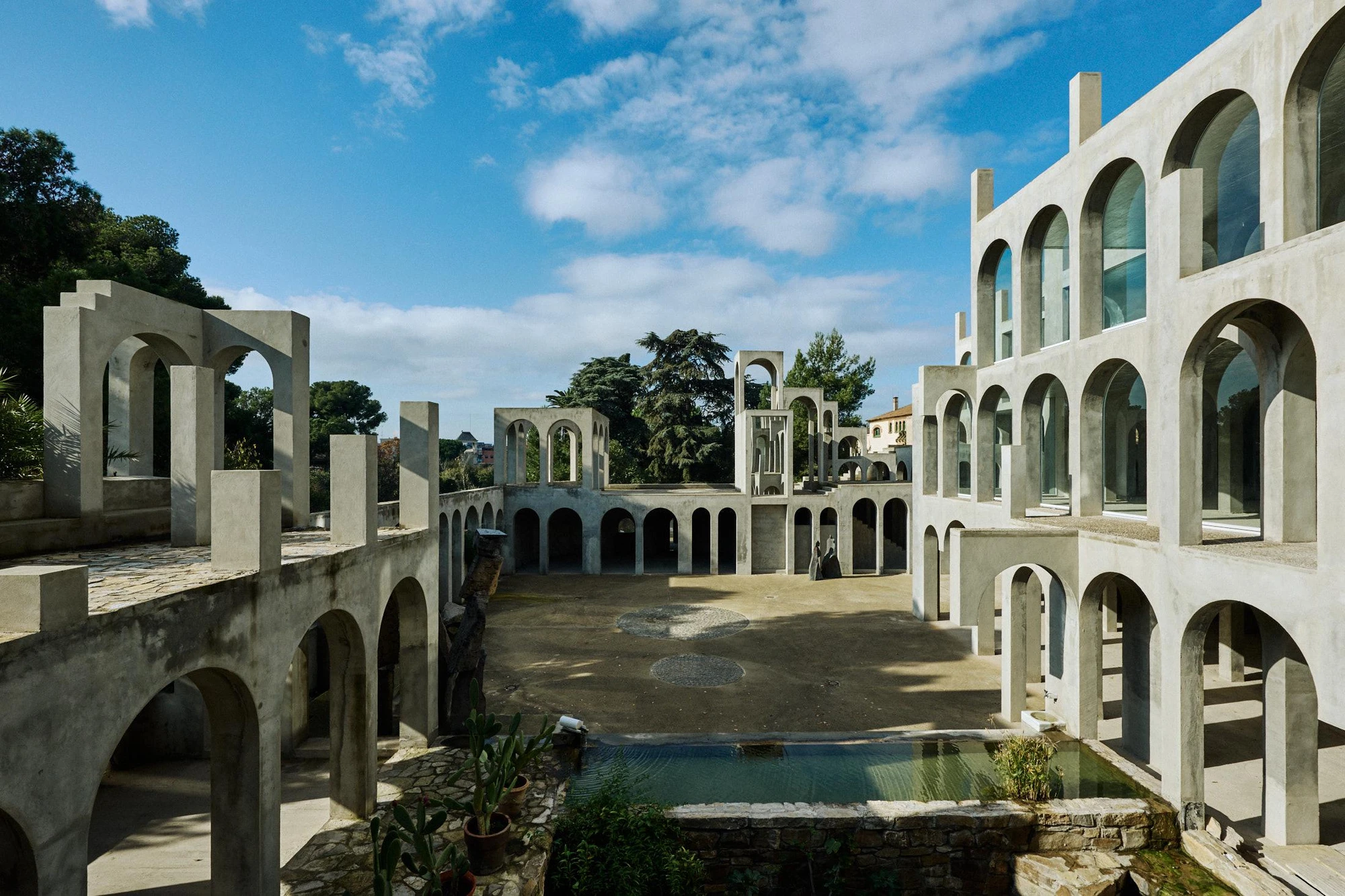 Xavier Corberó House and Studio by Xavier Corberó, photographed by Daniel Schäfer — Layered concrete arcades and a tall free-standing arch tower catch deep afternoon light across the compound's stepped roofs.