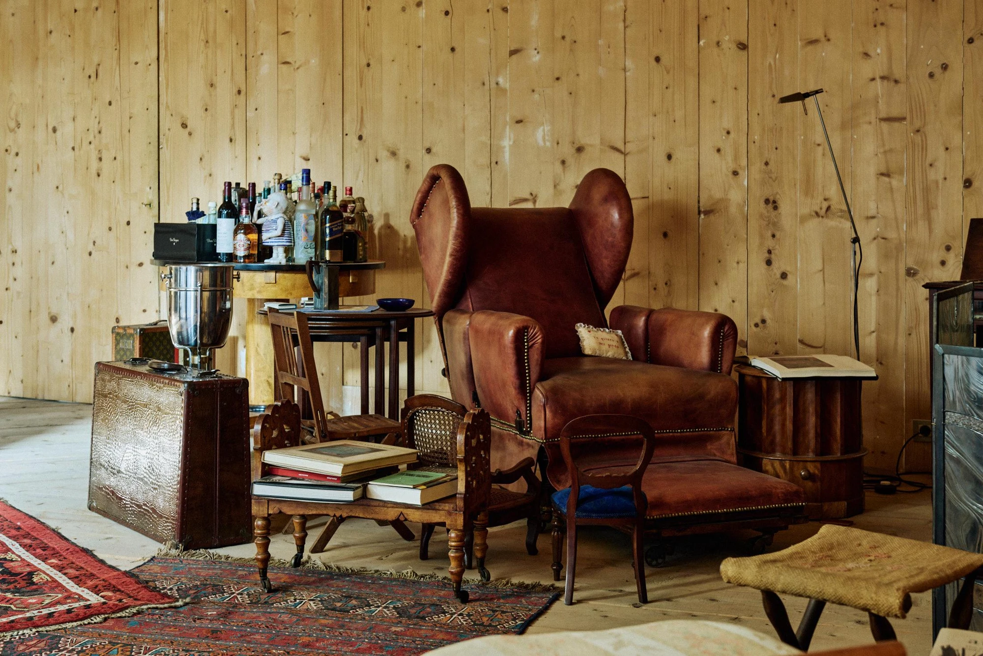 Xavier Corberó House and Studio by Xavier Corberó, photographed by Daniel Schäfer — A pine-panelled corner holds two oxblood leather wingback chairs and a makeshift bar of bottles on an old trunk, kilims layered over the floor.
