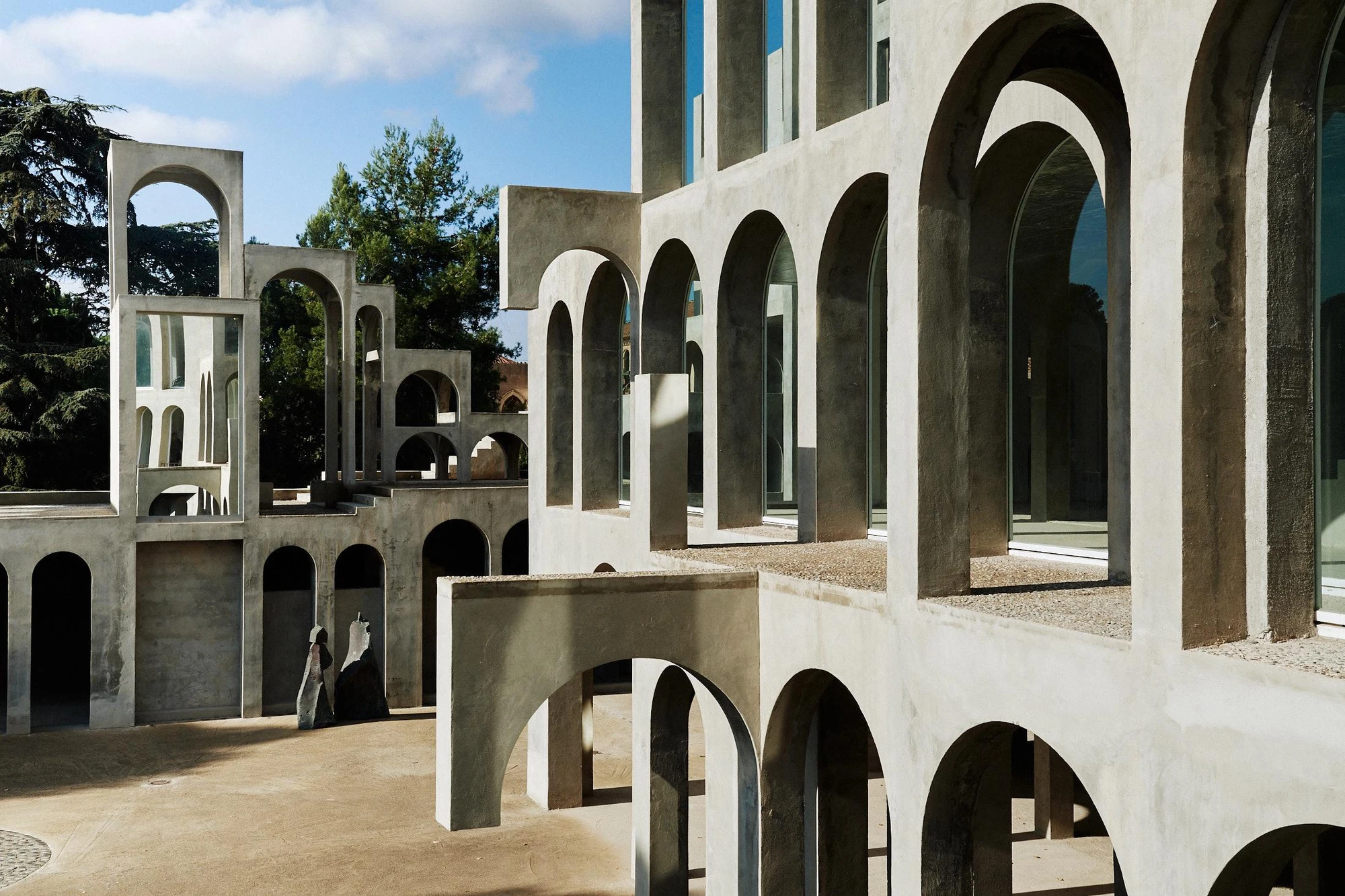 Xavier Corberó House and Studio by Xavier Corberó, photographed by Daniel Schäfer — A three-storey grid of glazed arches climbs at the right while a reed-edged reflecting pool holds the foreground and free-standing arch towers recede left.