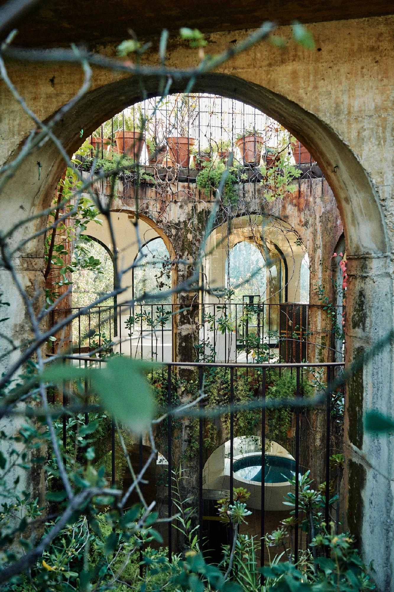 Xavier Corberó House and Studio by Xavier Corberó, photographed by Daniel Schäfer — Seen through bare branches, weathered plaster arches ring a planted court, terracotta pots lining a rail above a small plunge pool.