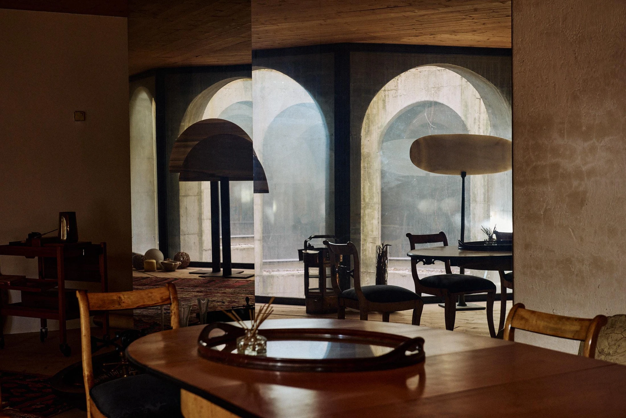 Xavier Corberó House and Studio by Xavier Corberó, photographed by Daniel Schäfer — A dim dining room of dark timber tables and dome pendant lamps opens through glazed arches onto the concrete courtyard beyond.