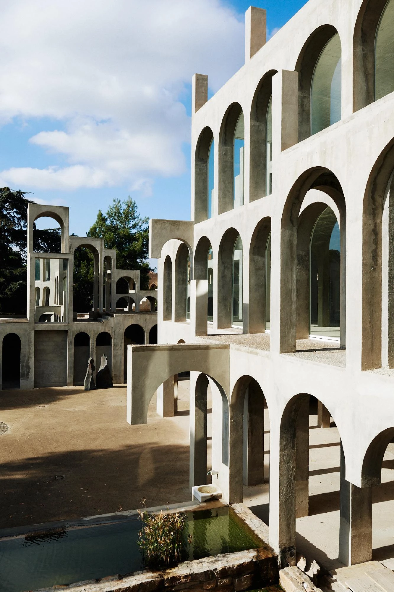 Xavier Corberó House and Studio by Xavier Corberó, photographed by Daniel Schäfer — The arched tower cluster seen vertically, a dark monolithic sculpture and a hooded stone form standing on the gravel forecourt below.