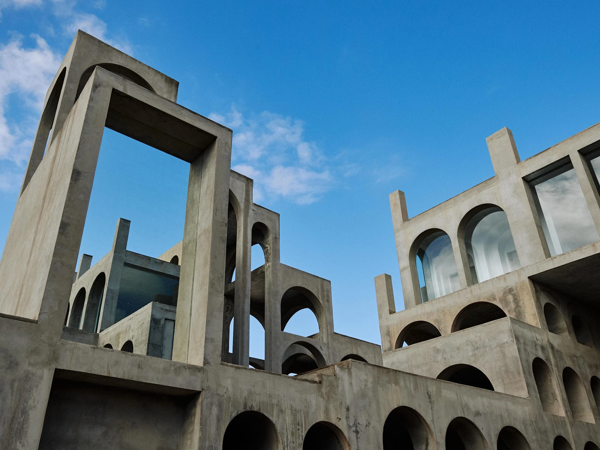 Xavier Corberó House and Studio by Xavier Corberó, photographed by Daniel Schäfer — A frontal three-storey block of glazed round arches under hard blue sky, a sun flare burning in one pane above the shadowed ground arcade.