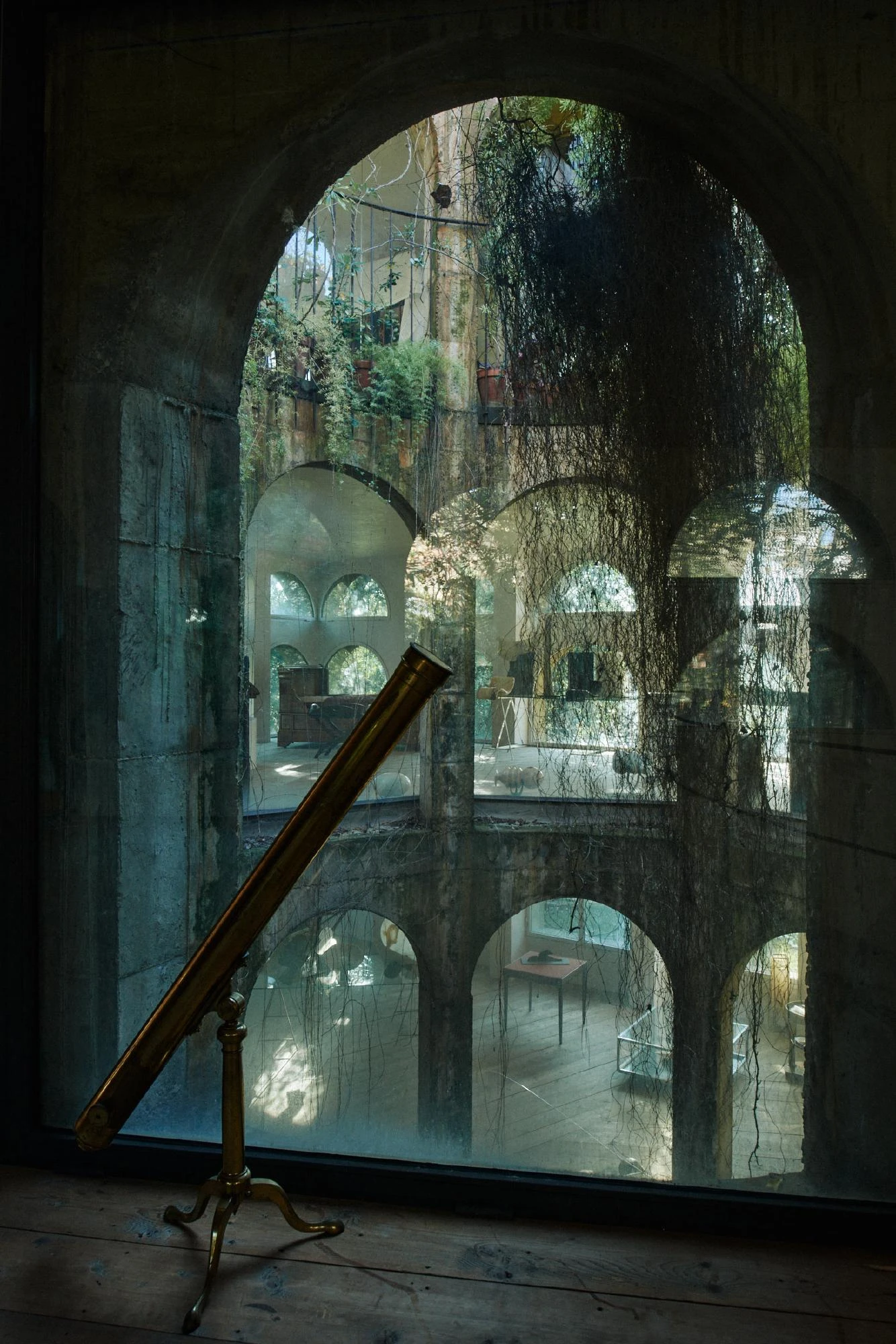 Xavier Corberó House and Studio by Xavier Corberó, photographed by Daniel Schäfer — A brass telescope on a tripod stands at a vine-hung arched window, looking down through the glass into the tiered arcaded court below.