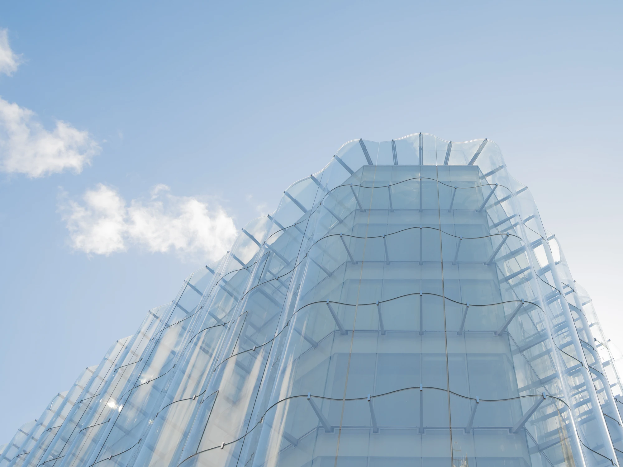 La Samaritaine by SANAA, photographed by Jared Chulski — Looking up the corner, the glass panes bend into shallow vertical waves against a clear blue sky.