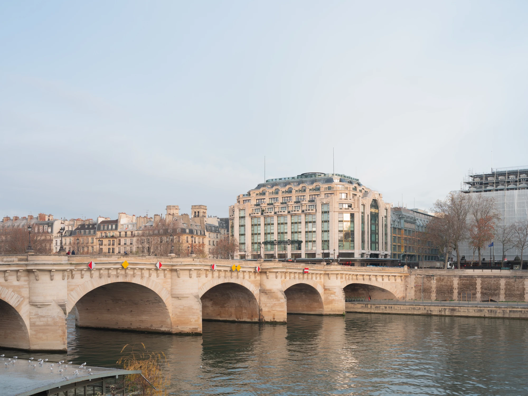 La Samaritaine by SANAA, photographed by Jared Chulski — Seen from across the Seine over the Pont Neuf, Henri Sauvage's stone building holds the river frontage.