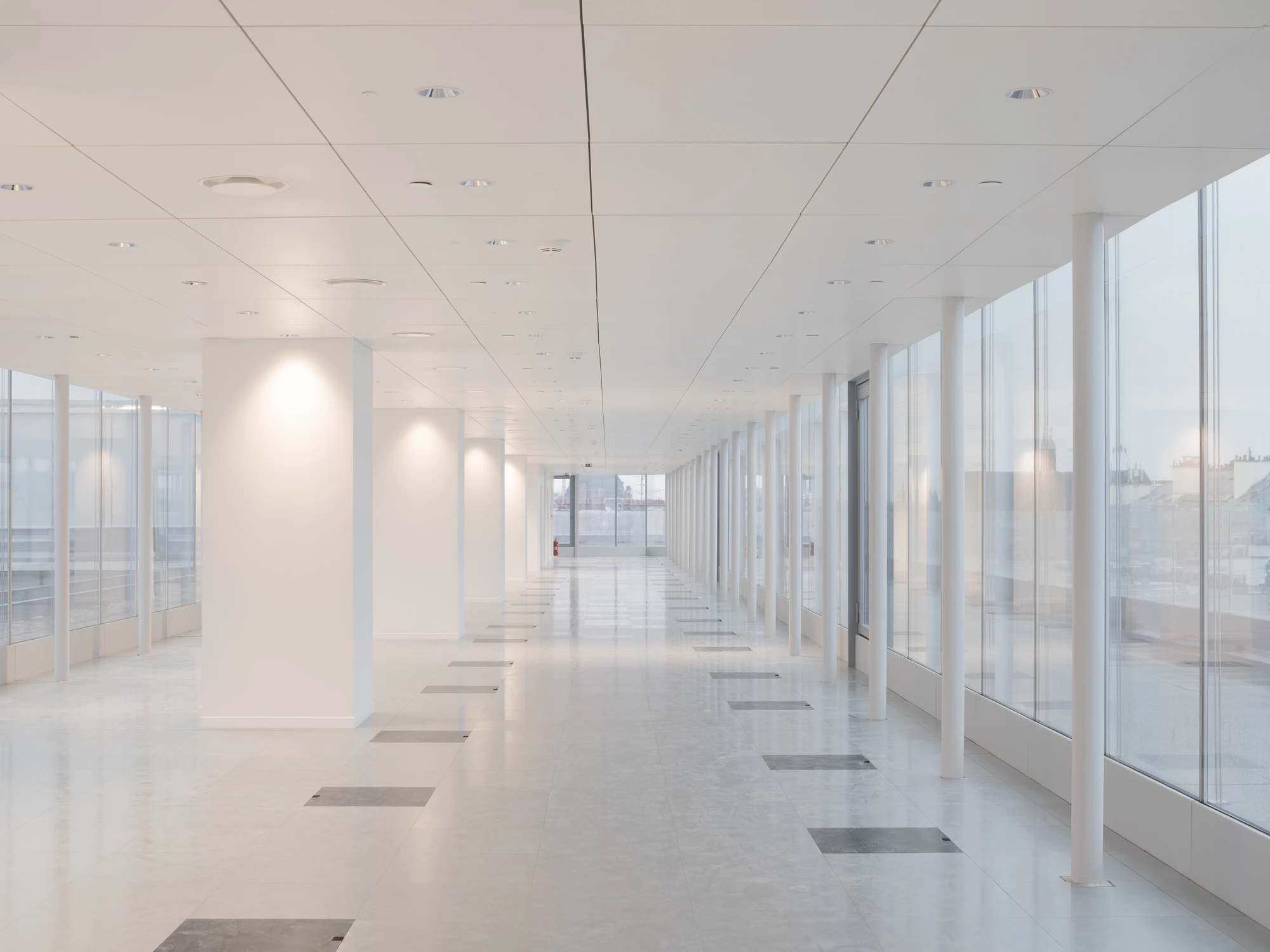 La Samaritaine by SANAA, photographed by Jared Chulski — A contemporary office floor in white, slender columns lining a glass wall that opens to the Paris rooftops.