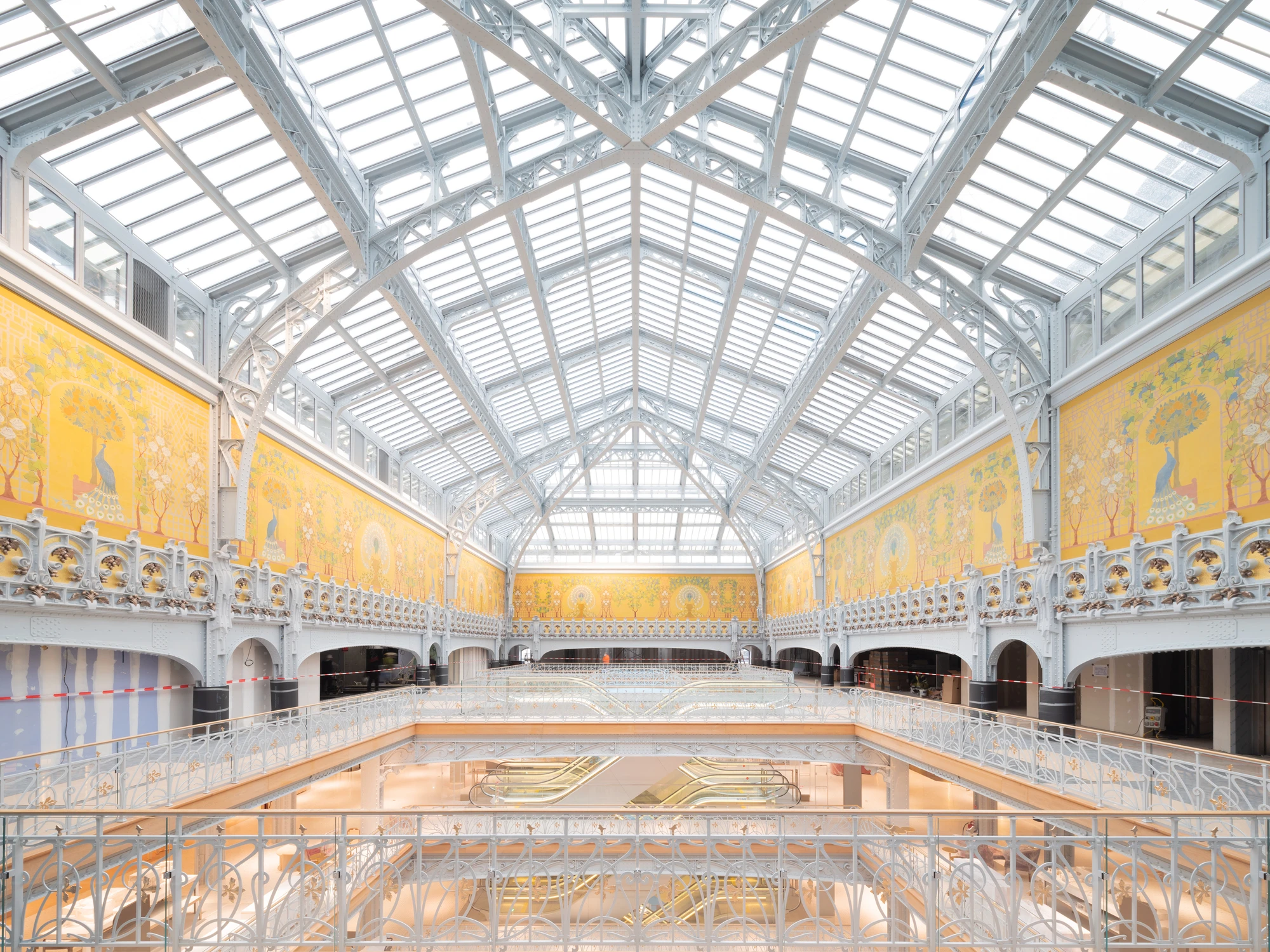 La Samaritaine by SANAA, photographed by Jared Chulski — The symmetry of Frantz Jourdain's hall, iron balconies rising to the glass roof under the golden mural band.
