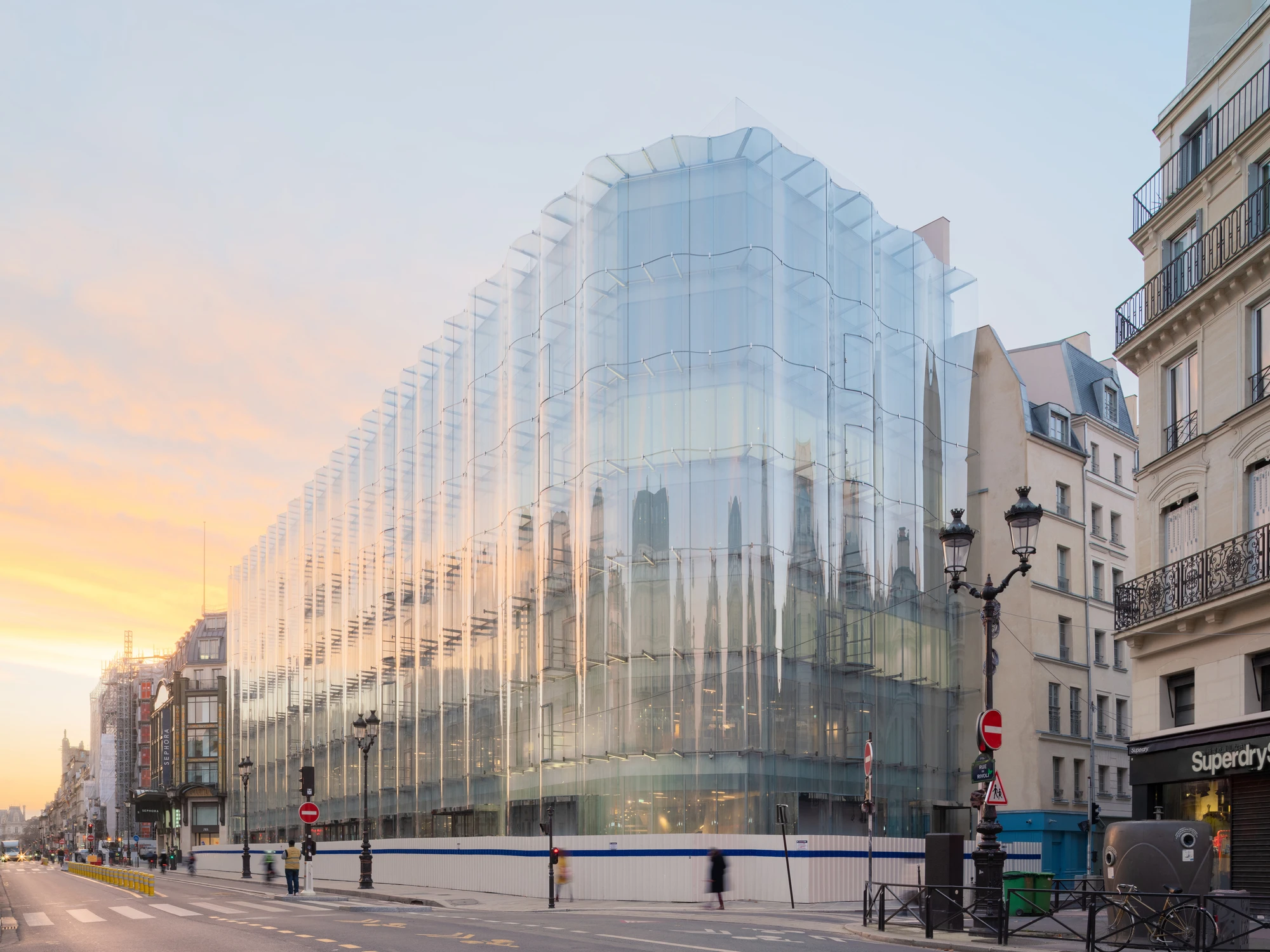 La Samaritaine by SANAA, photographed by Jared Chulski — Sunset behind the block, the rippling glass facade catching orange light above the street lamps.