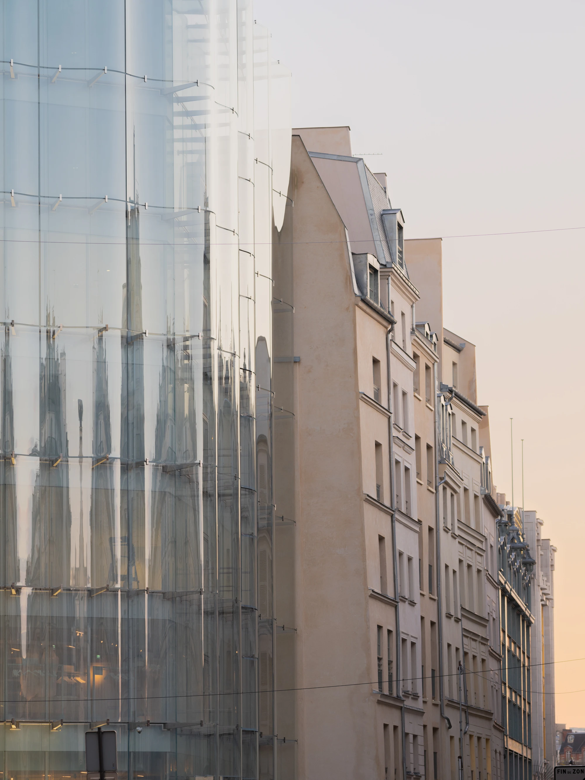 La Samaritaine by SANAA, photographed by Jared Chulski — Curved glass meets the flat stone flank of a neighbouring Parisian building, the two surfaces caught in warm low sun.