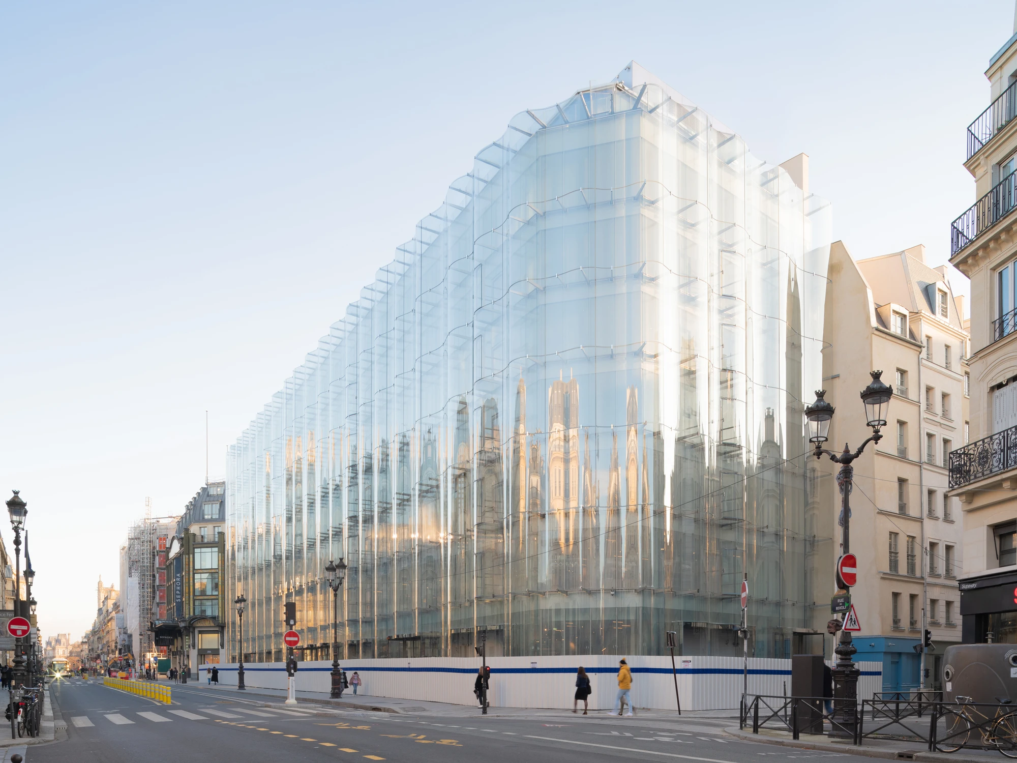 La Samaritaine by SANAA, photographed by Jared Chulski — The building reads as a translucent wedge on the corner, curved glass rising over the empty morning street beside a Haussmann block.