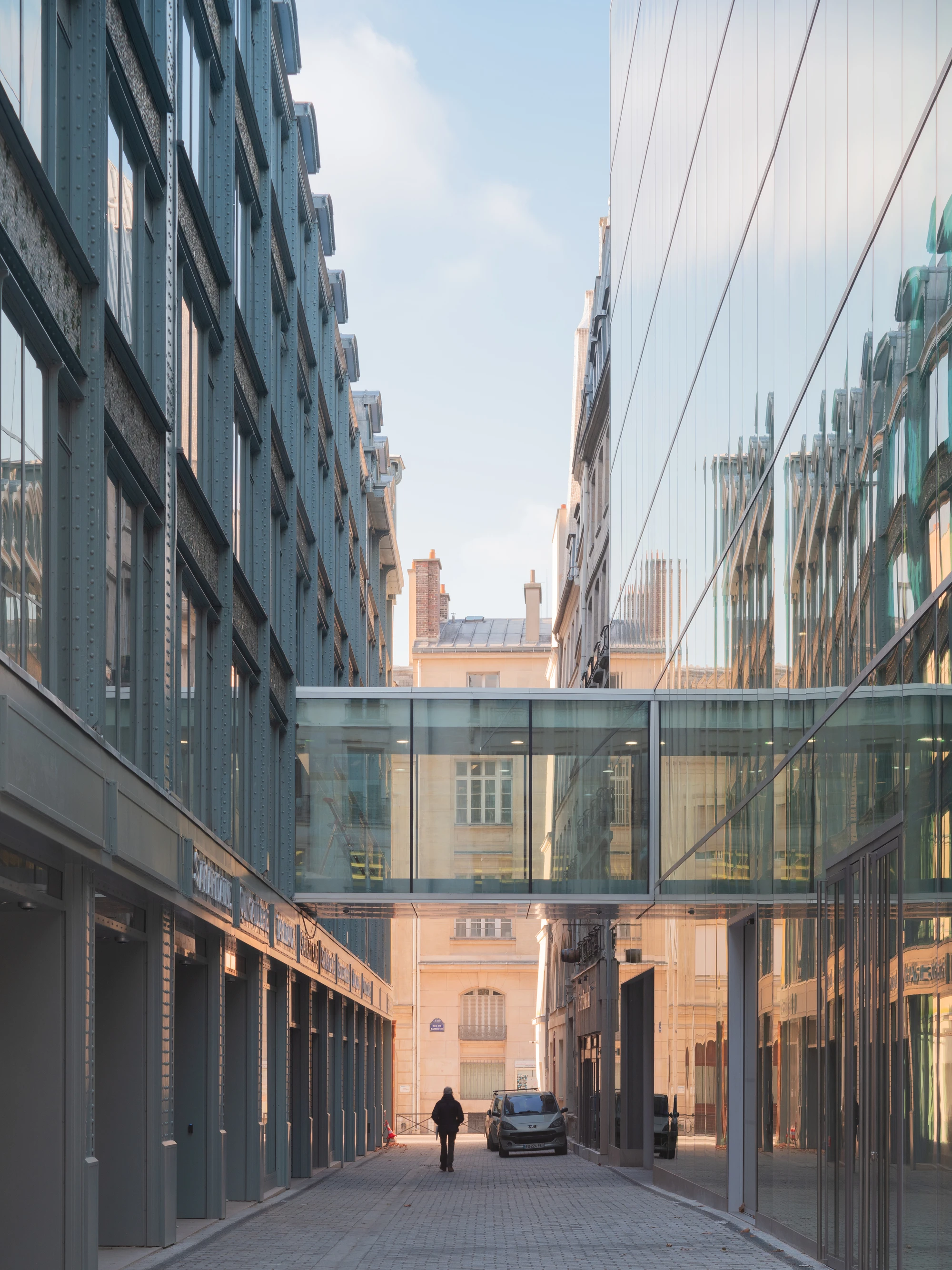 La Samaritaine by SANAA, photographed by Jared Chulski — The new passage cut through the block, a glazed link bridge crossing overhead and a single figure in the sunlit lane.