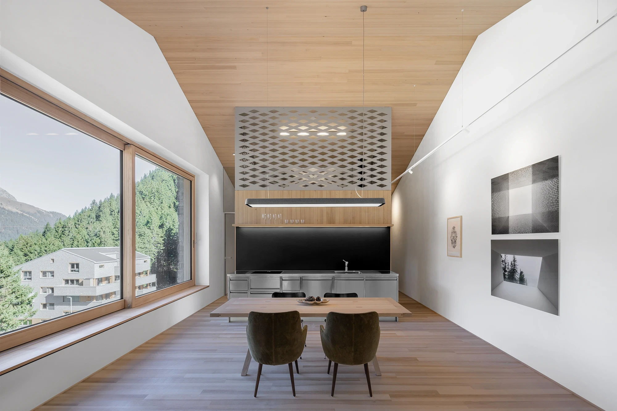 Vergalderie by Christian Tonko, photographed by Gustav Willeit — The loft kitchen in stainless steel below a perforated diamond screen, white fir ceiling sloping to the plaster wall