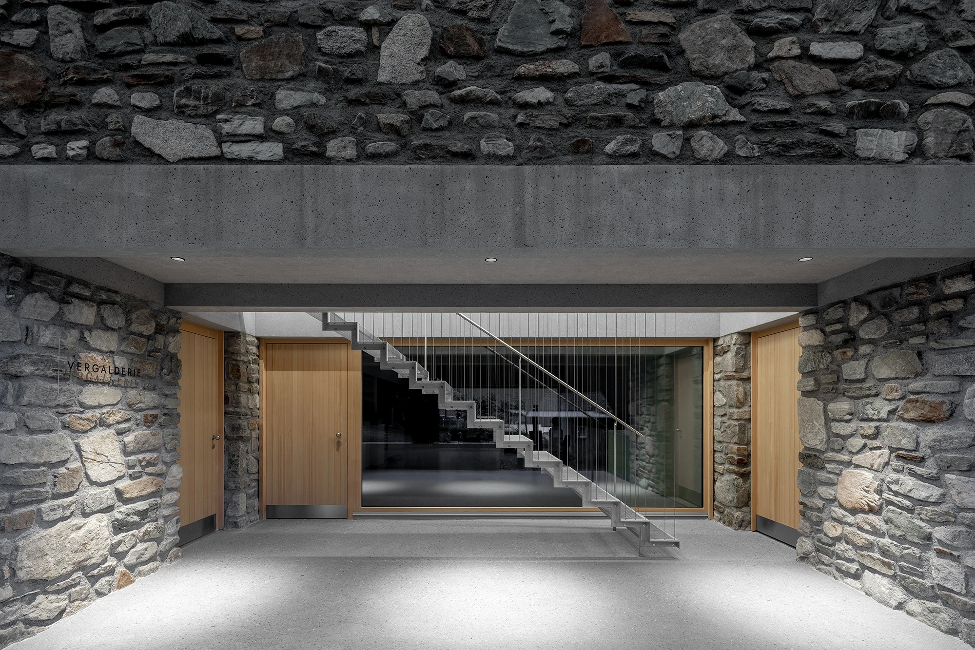 Vergalderie by Christian Tonko, photographed by Gustav Willeit — The frontal entry portal under its concrete beam, twin timber doors flanking a cantilevered concrete stair strung with thin steel rods