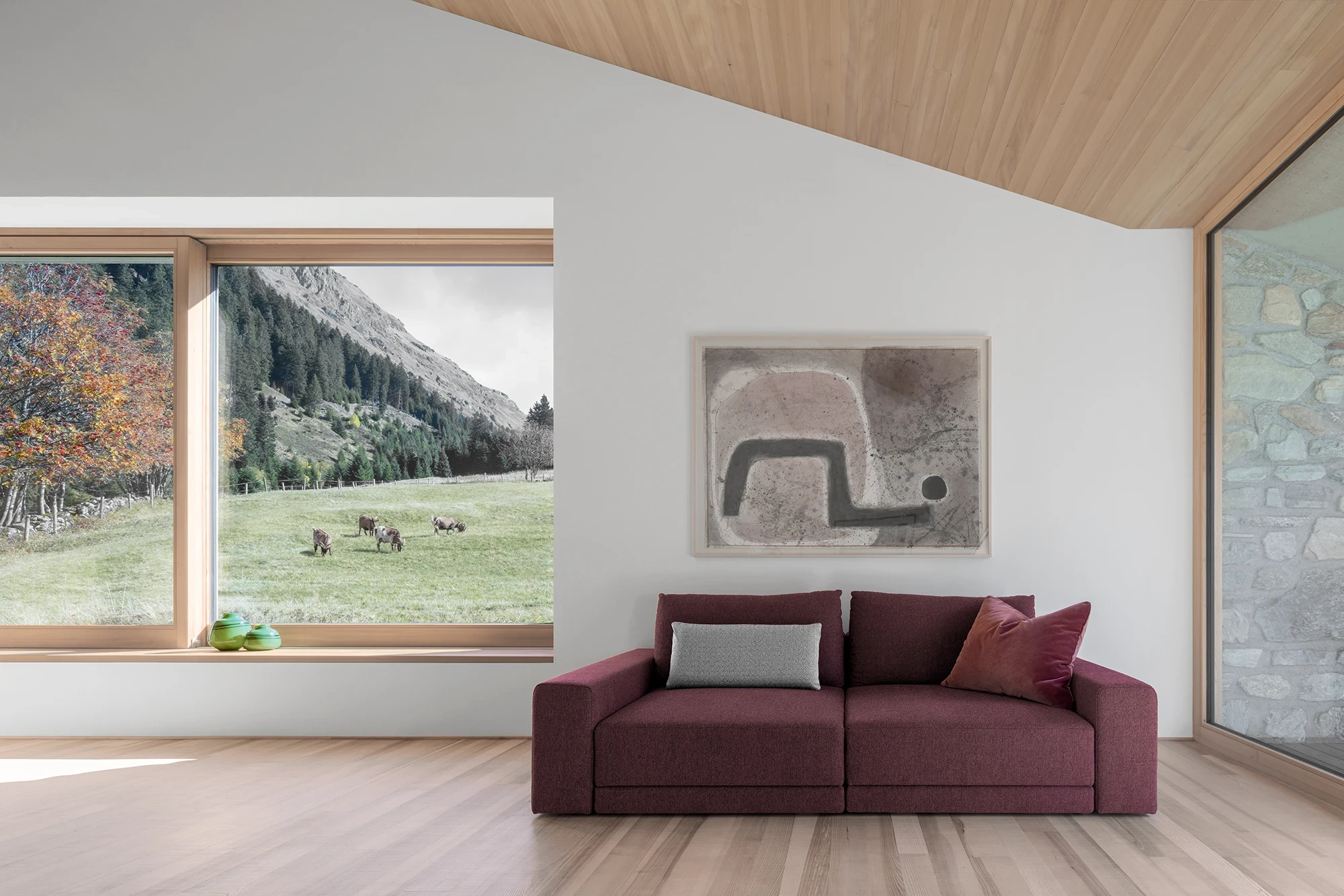 Vergalderie by Christian Tonko, photographed by Gustav Willeit — A burgundy sofa under an abstract work, the deep timber-lined window framing cows at pasture on the far slope