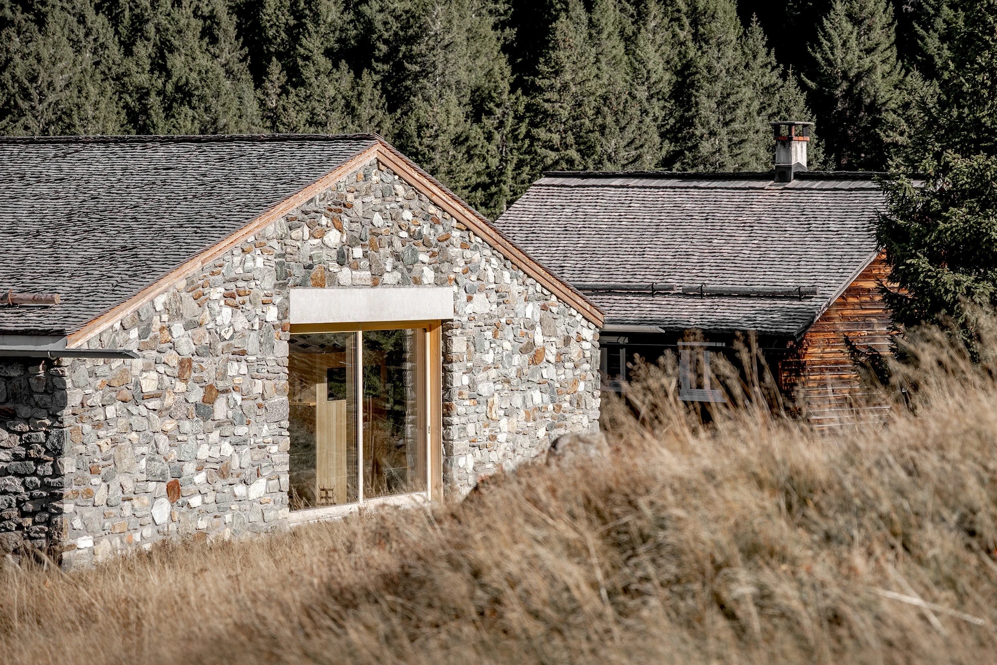 Vergalderie by Christian Tonko, photographed by Gustav Willeit — A close view of the eaves, where hand-laid stone meets a larch-lined opening and the dry autumn grass of the meadow