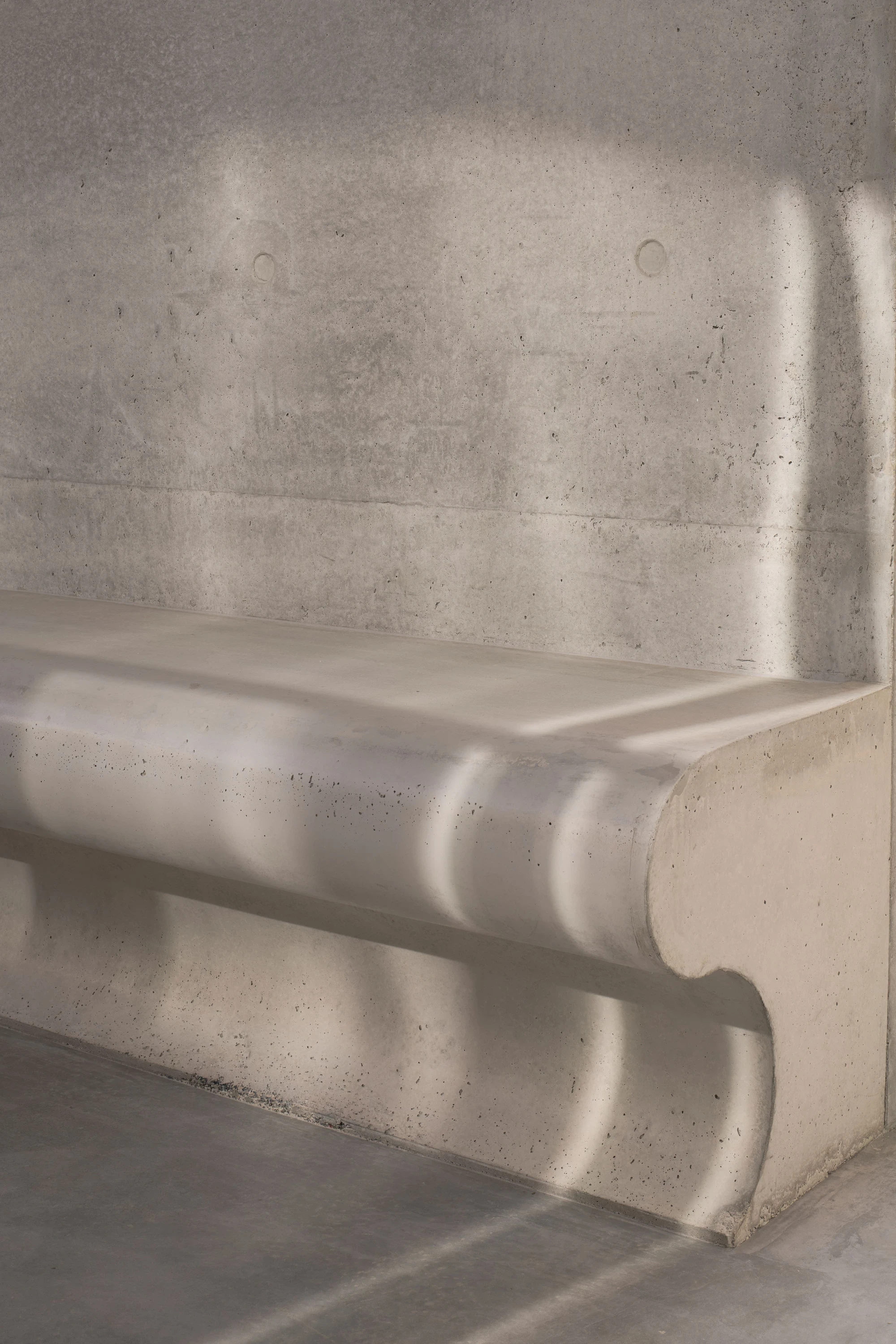 Gallery For A Tree Flyover Marcellin College by Farrell Wray Architects — Braybrook, Australia: the cast concrete bench with its scrolled profile, dappled light falling across the board-marked wall.
