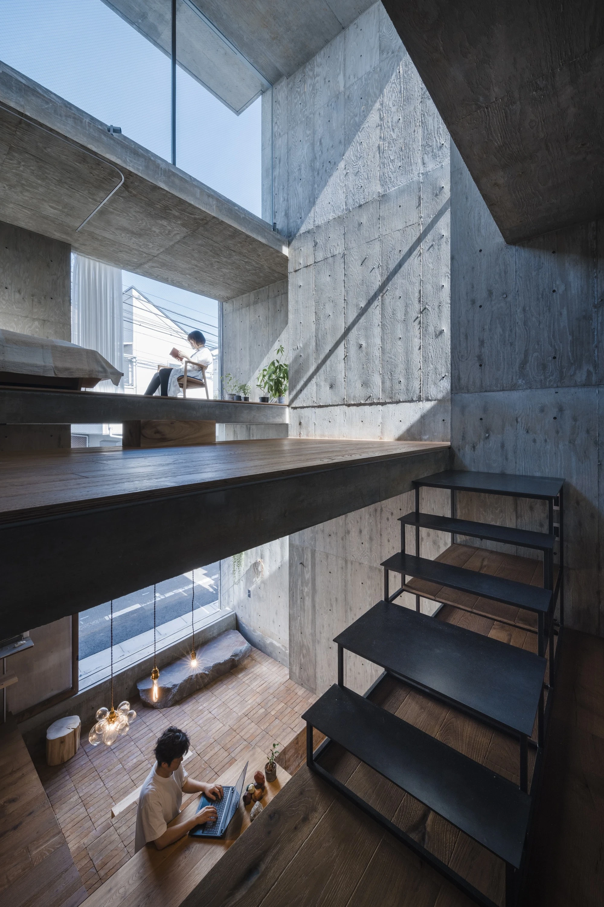 Building Frame of the House by IGArchitects, Japan — a tall section cut by daylight from a high north opening, with residents reading and working across two offset concrete floors.