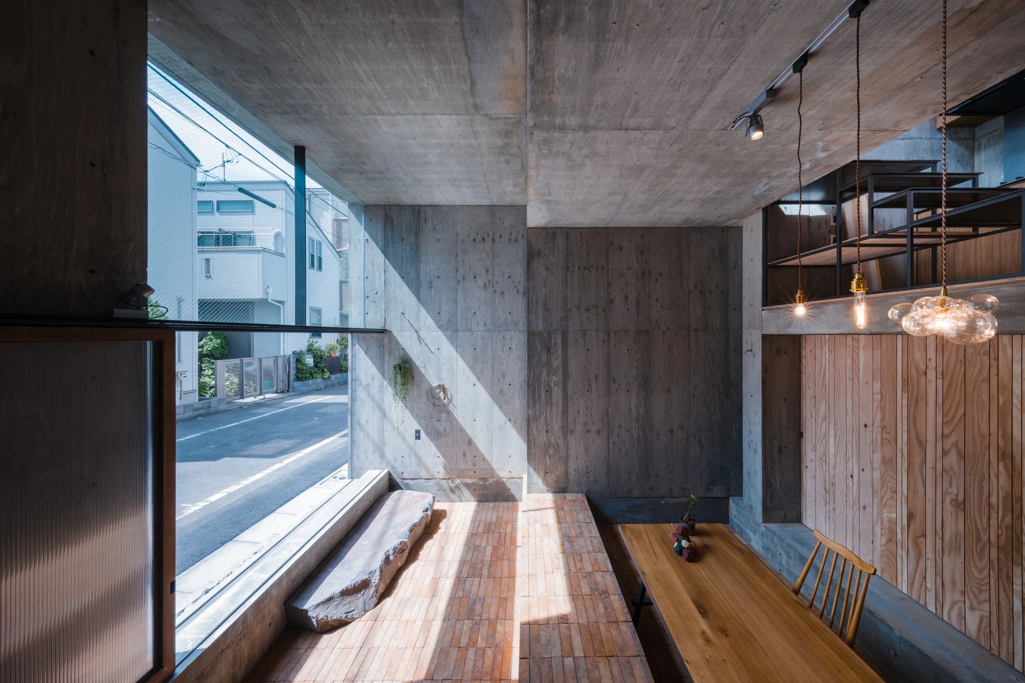 Building Frame of the House by IGArchitects, Japan — a low stone bench and terracotta-brick floor at a full-height street window, sunlight raking across board-formed concrete.