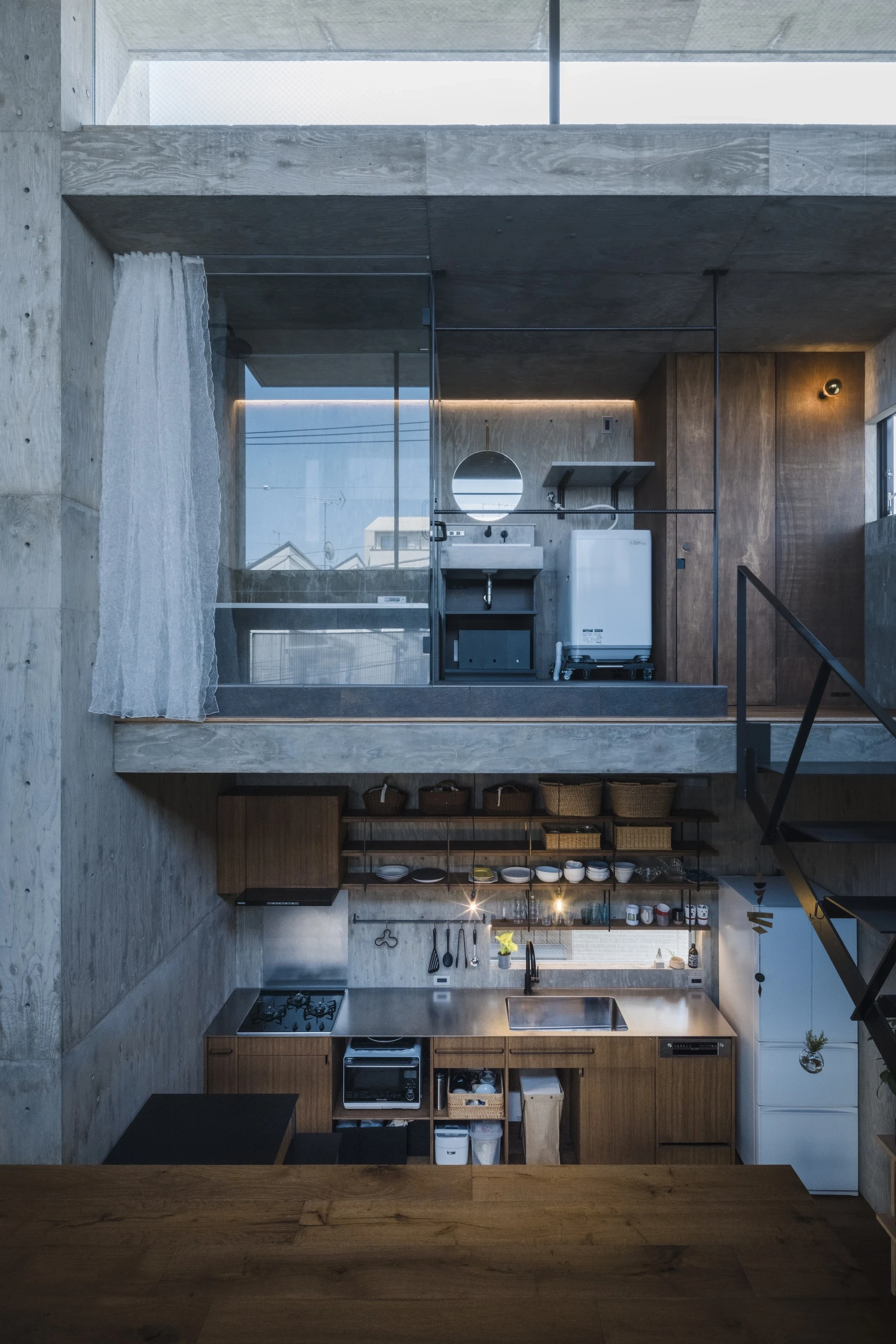 Building Frame of the House by IGArchitects, Japan — a compact stainless kitchen tucked beneath a glazed mezzanine bath, the whole section reading top to bottom in one concrete volume.