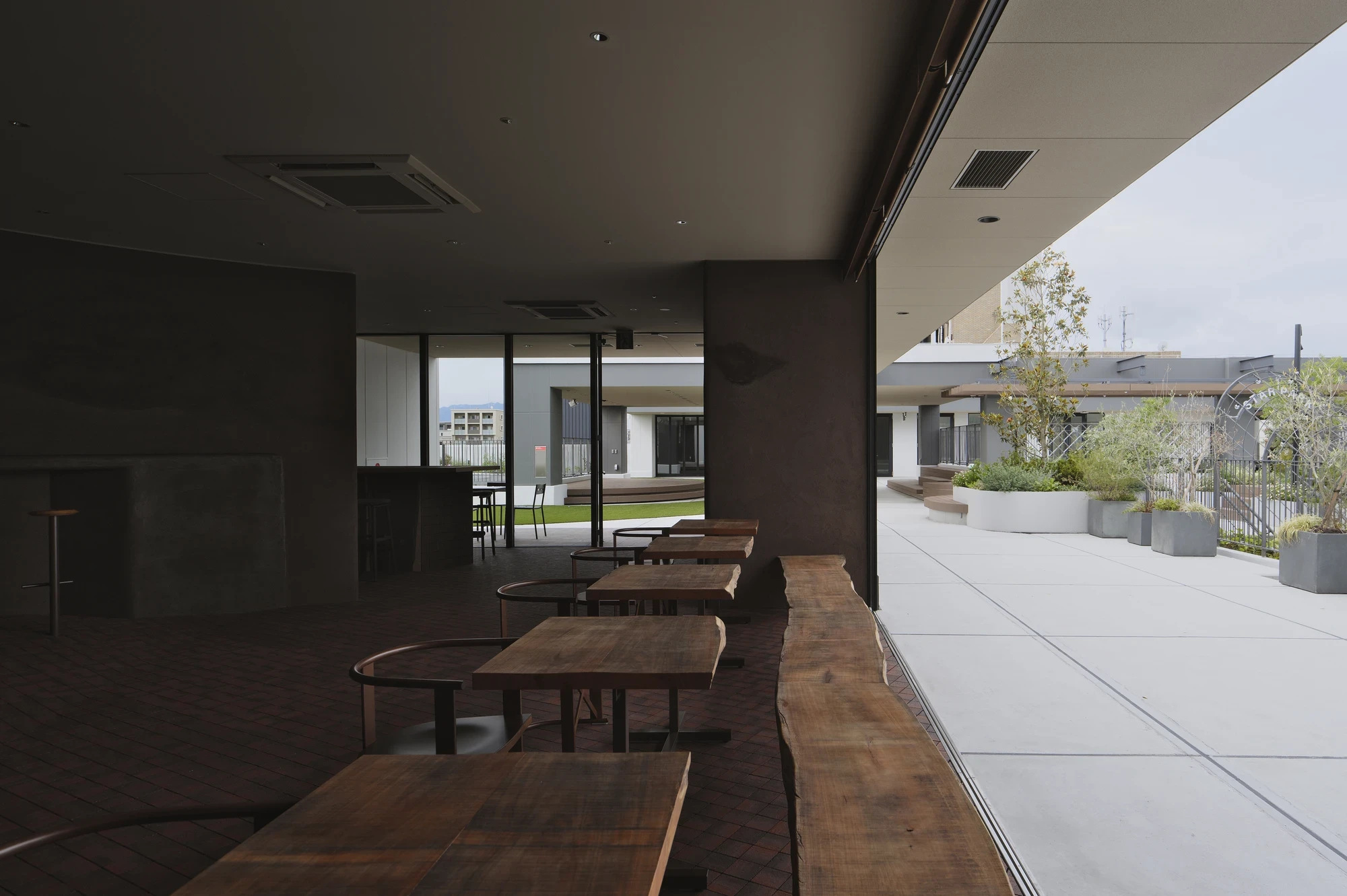 NIWA FUKUOKA by ANONIMAL design community — Fukuoka, Japan: raw timber benches line the glazed edge where the interior meets the concrete rooftop plaza and its planting.