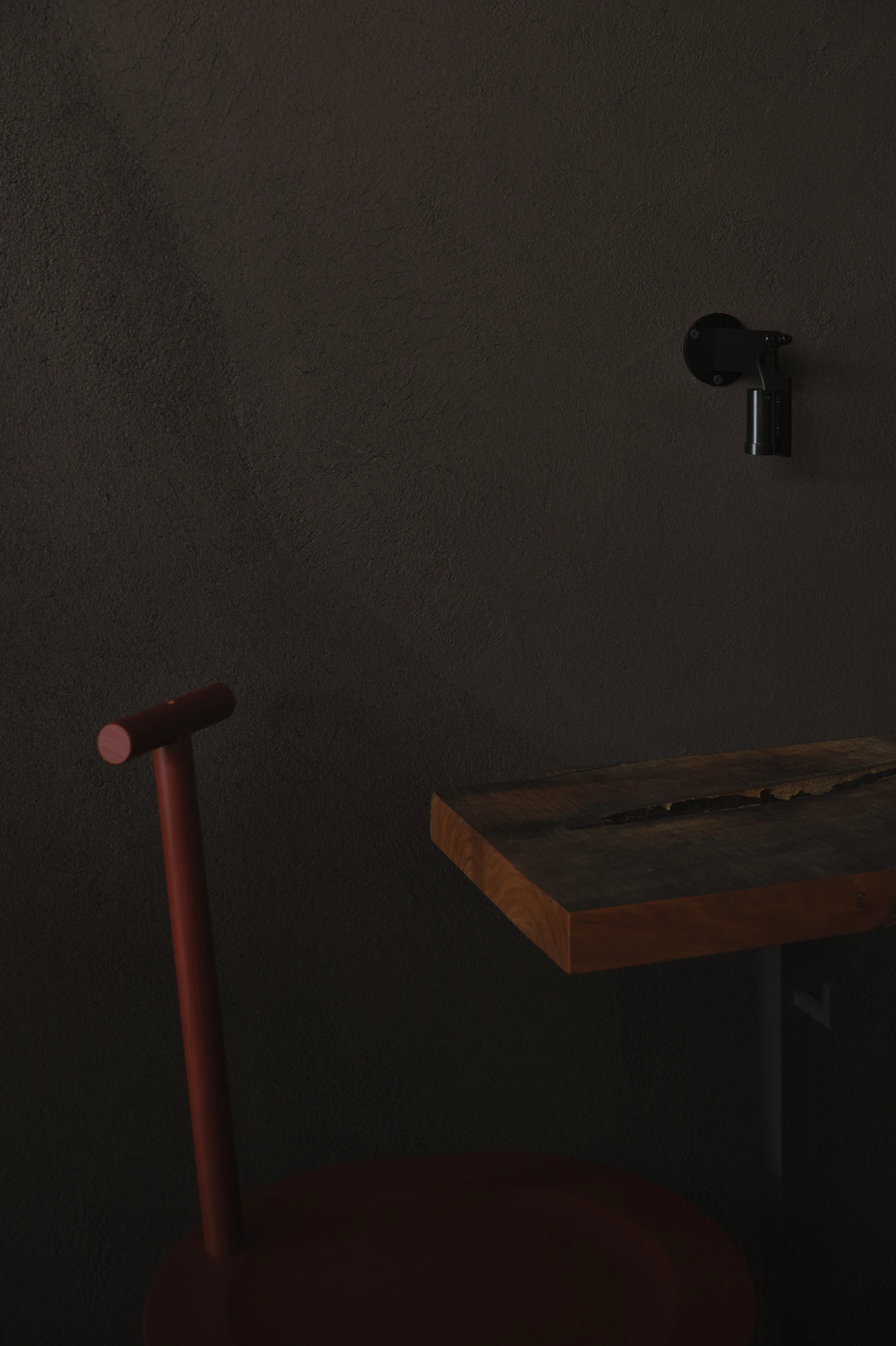 NIWA FUKUOKA by ANONIMAL design community — Fukuoka, Japan: a close view of a live-edge timber tabletop against earthen plaster, an oxblood chair and a black wall fitting caught in low light.