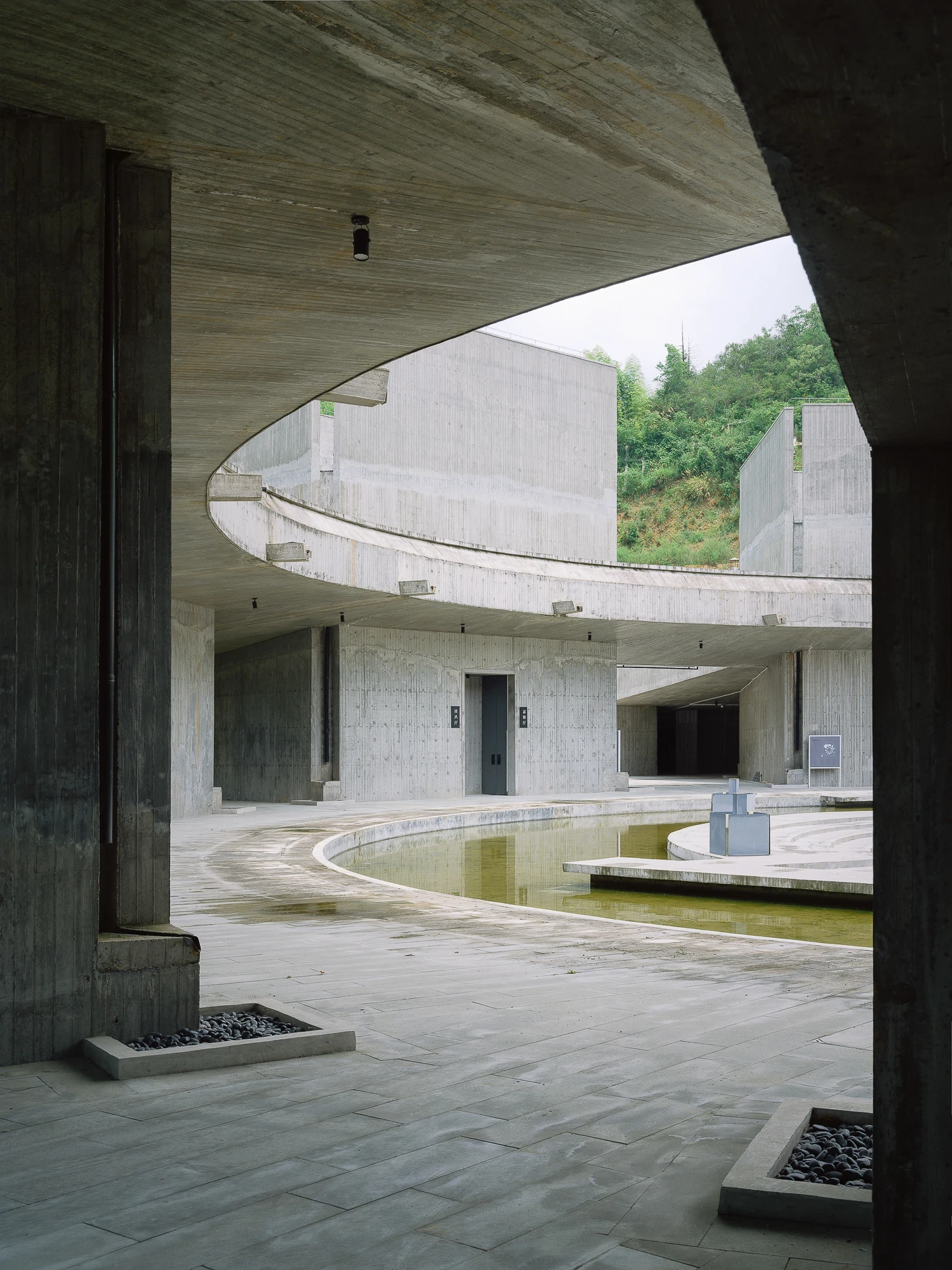 Suichang Funerary Complex by Untitled Architects, photographed by Tianzhou Yang — a curving concrete ramp and balustrade wrap a sunken court around a still pool below.