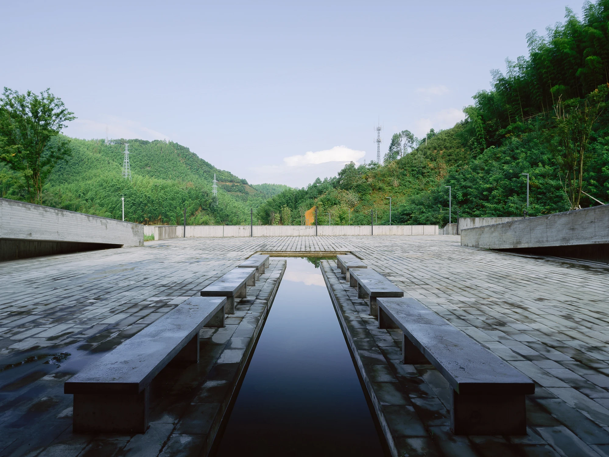Suichang Funerary Complex by Untitled Architects, photographed by Tianzhou Yang — stone benches line a long water channel running through a paved court toward the wooded hillside.