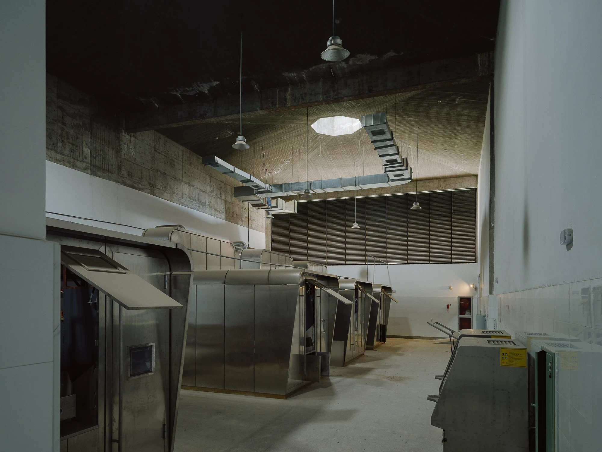 Suichang Funerary Complex by Untitled Architects, photographed by Tianzhou Yang — a row of stainless steel cremation furnaces under pendant lamps in a whitewashed working hall.