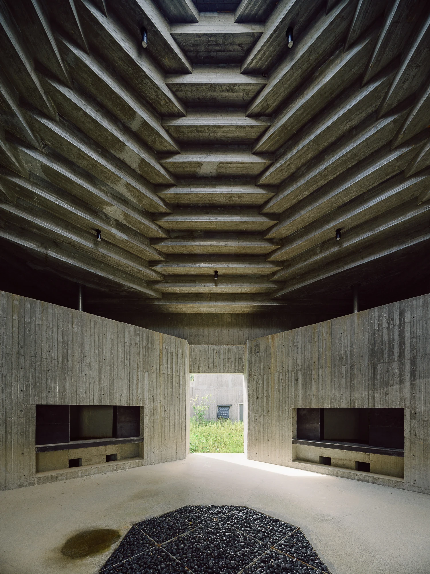 Suichang Funerary Complex by Untitled Architects, photographed by Tianzhou Yang — a corbelled concrete ceiling steps down over a hall with recessed niches and a round bed of black stones on the floor.