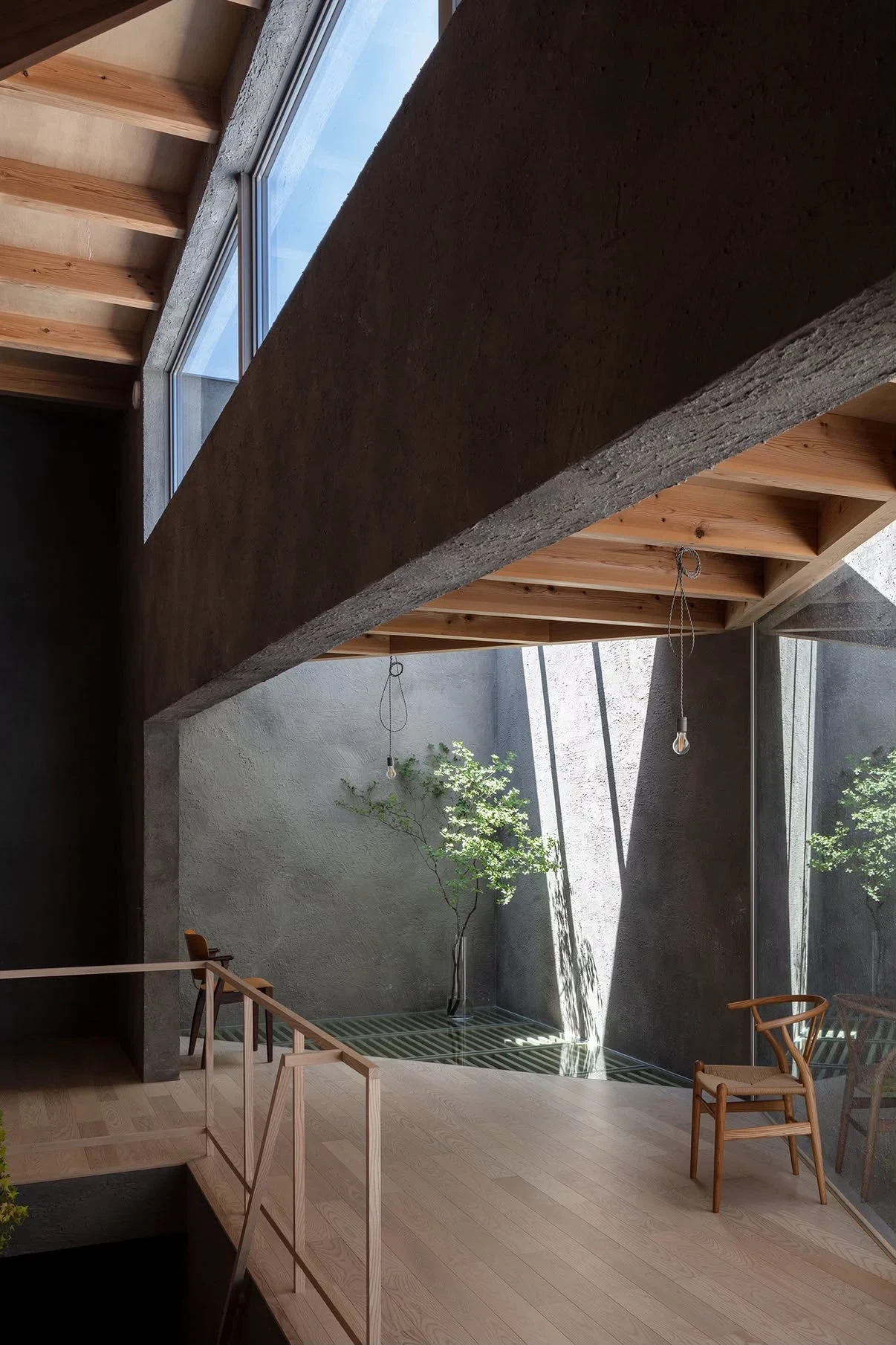 NesT by mA-style architects, photographed by Norihito Yamauchi — A concrete beam and cedar joists bridge over an oak-floored upper level, sunlight striping the grey plaster wall through a glazed courtyard.