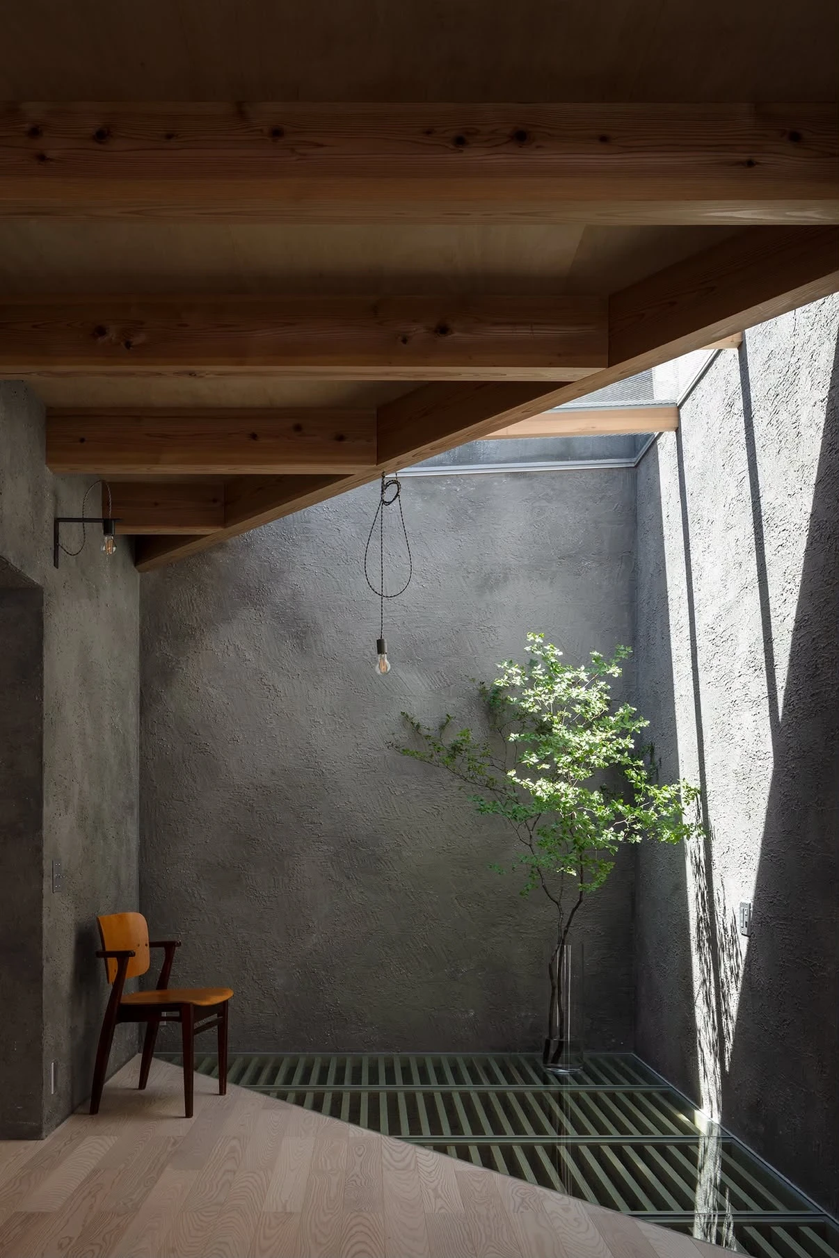 NesT by mA-style architects, photographed by Norihito Yamauchi — A pale wood chest and concrete console stand on a polished floor between troweled grey walls, sun patterning the render through a louvred opening.
