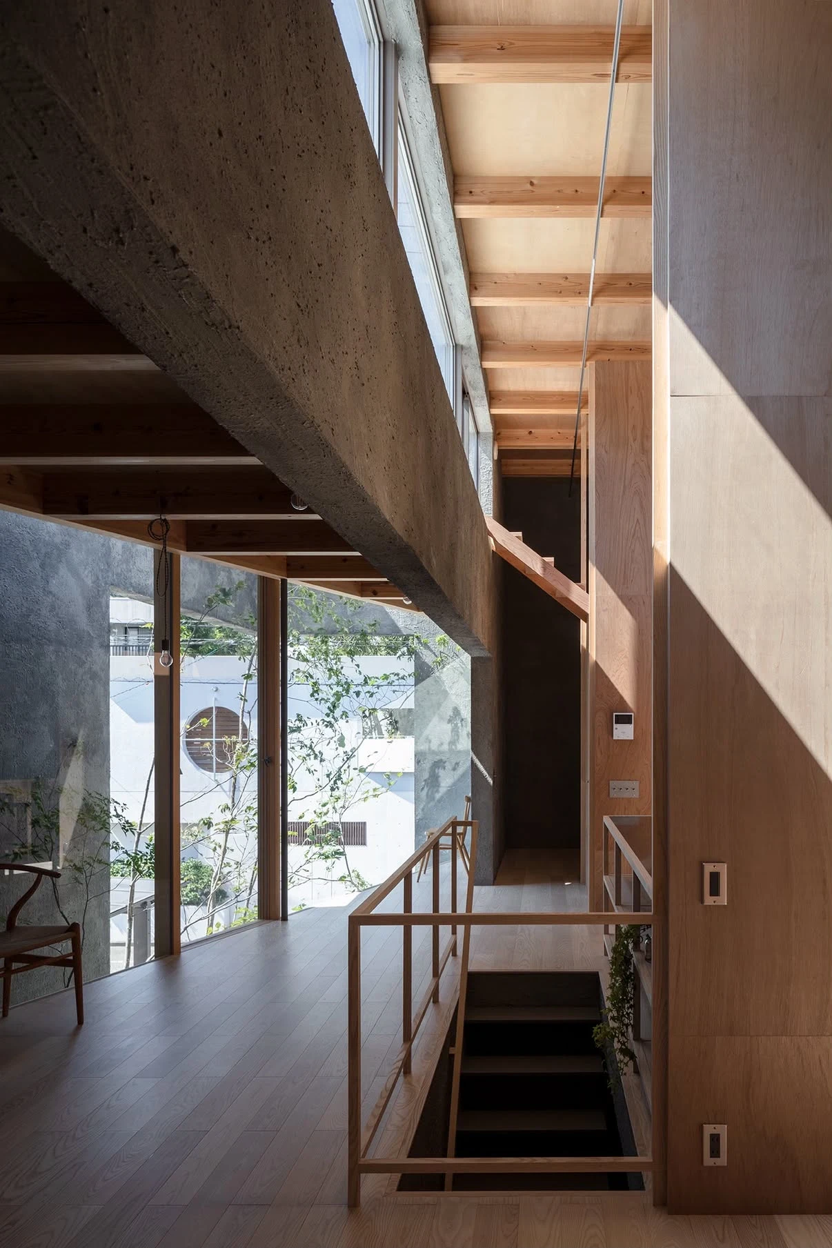 NesT by mA-style architects, photographed by Norihito Yamauchi — A yellow vintage chair sits under exposed cedar beams beside a courtyard tree, light dropping through grating onto grey plaster.