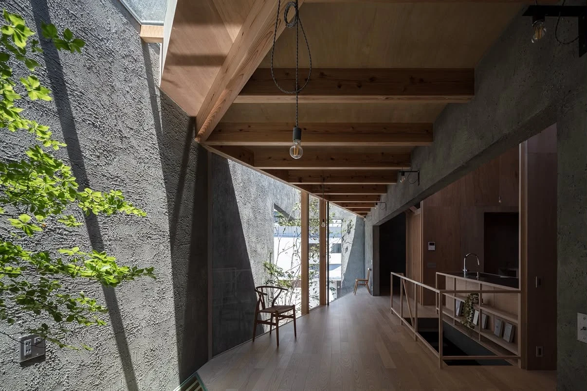 NesT by mA-style architects, photographed by Norihito Yamauchi — A window and open corner frame the hillside town of tiled houses, timber beams and grey render carrying the greenery of a courtyard inside.