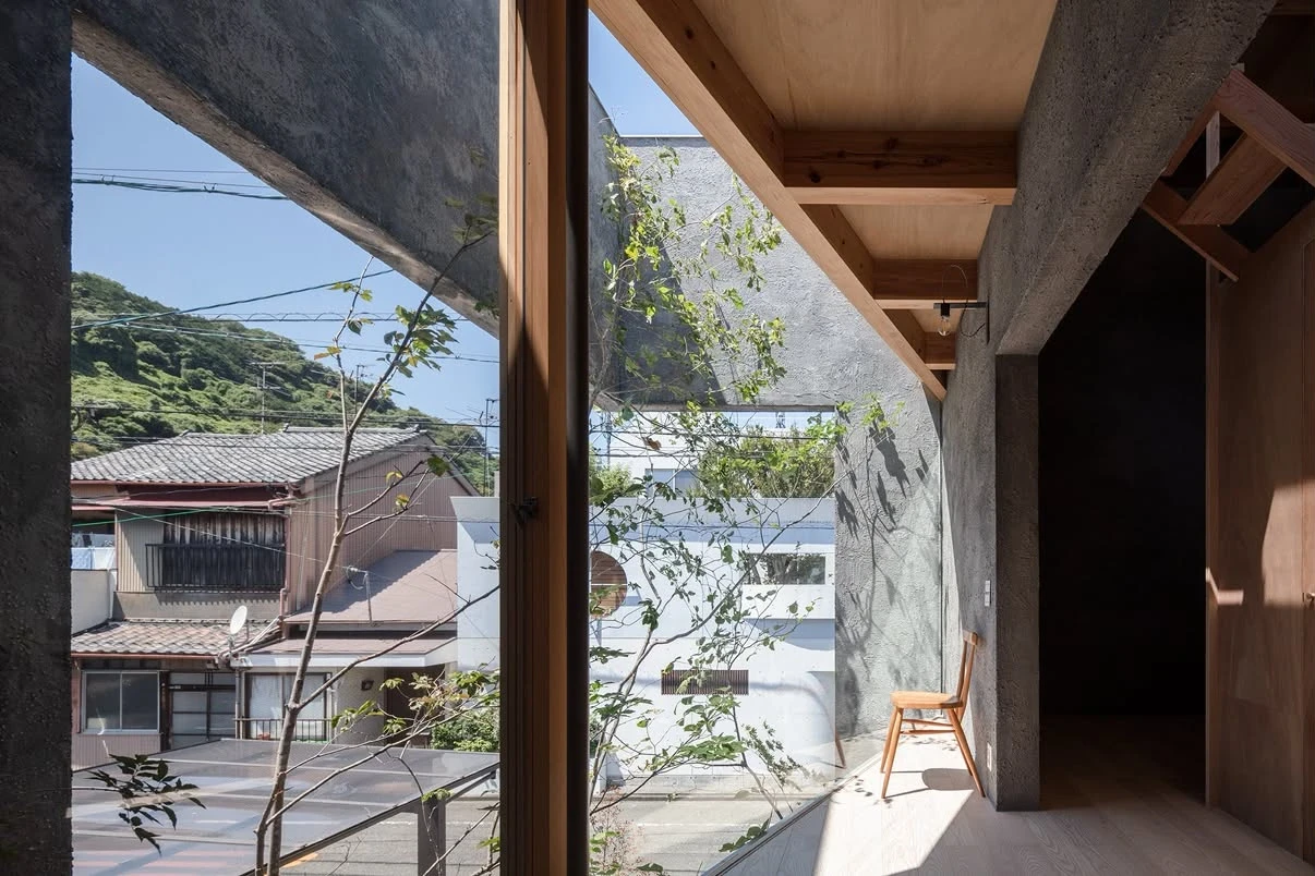 NesT by mA-style architects, photographed by Norihito Yamauchi — A double-height room where a board-formed concrete beam crosses beneath pale cedar joists, light falling onto steel grating and a courtyard tree.