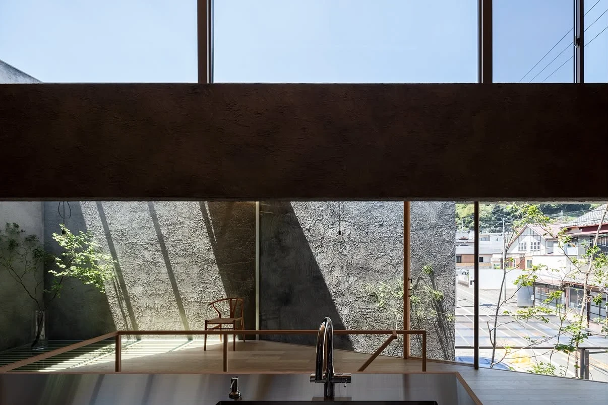 NesT by mA-style architects, photographed by Norihito Yamauchi — Seen over a kitchen sink, a wide window frames the grey rough-cast interior and the tiled roofs and hillside town beyond.