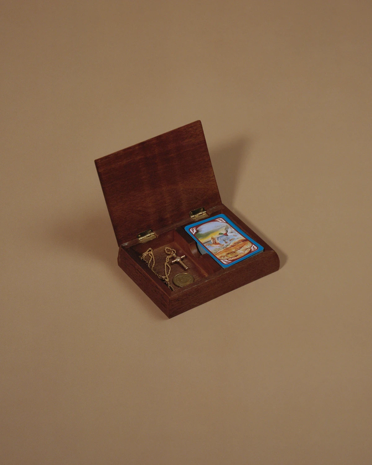 Wading by Jon Testa, photographed by Jon Testa — an open wooden box on seamless paper holding a gold cross on a chain, a coin, and a stack of prayer cards.