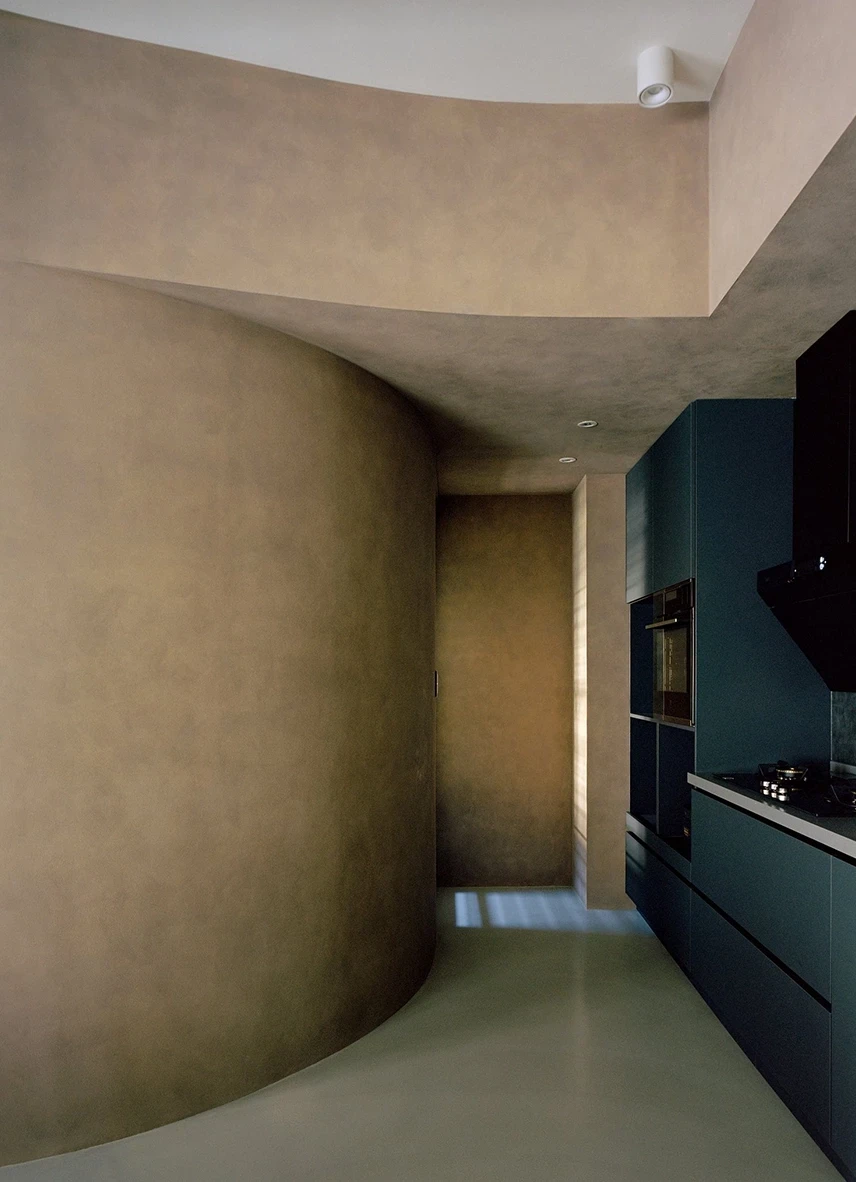 Uno's Purr-fect Time by W&Li Design, photographed by Studio Millspace — a curved plaster volume rounds into the circulation beside inky blue-black kitchen cabinetry and a built-in oven.