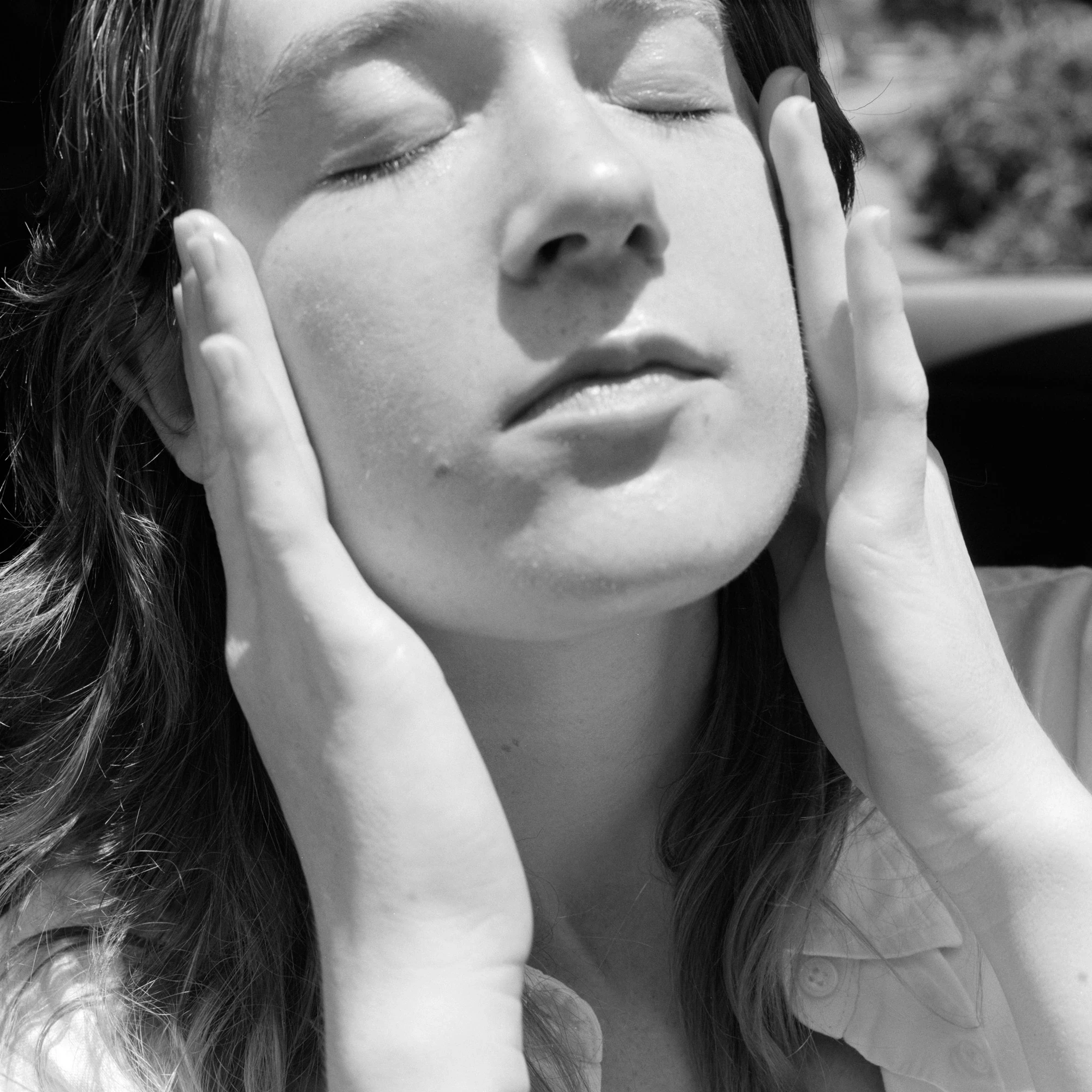 Eternal Return by Benjamin Young, photographed by Benjamin Young — a young woman cradles her own face in both hands, eyes closed, in full direct sun.