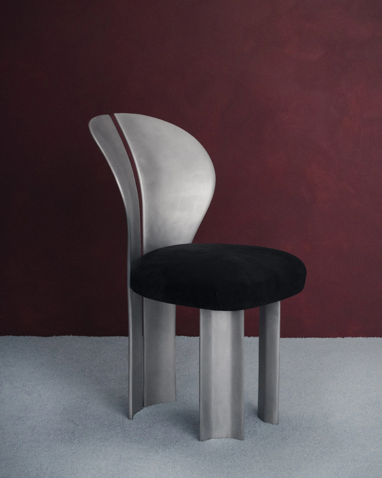 Lilium Chair by Studio NRG — a three-quarter view showing the split petal backrest in brushed satin aluminium above a rounded black suede seat.