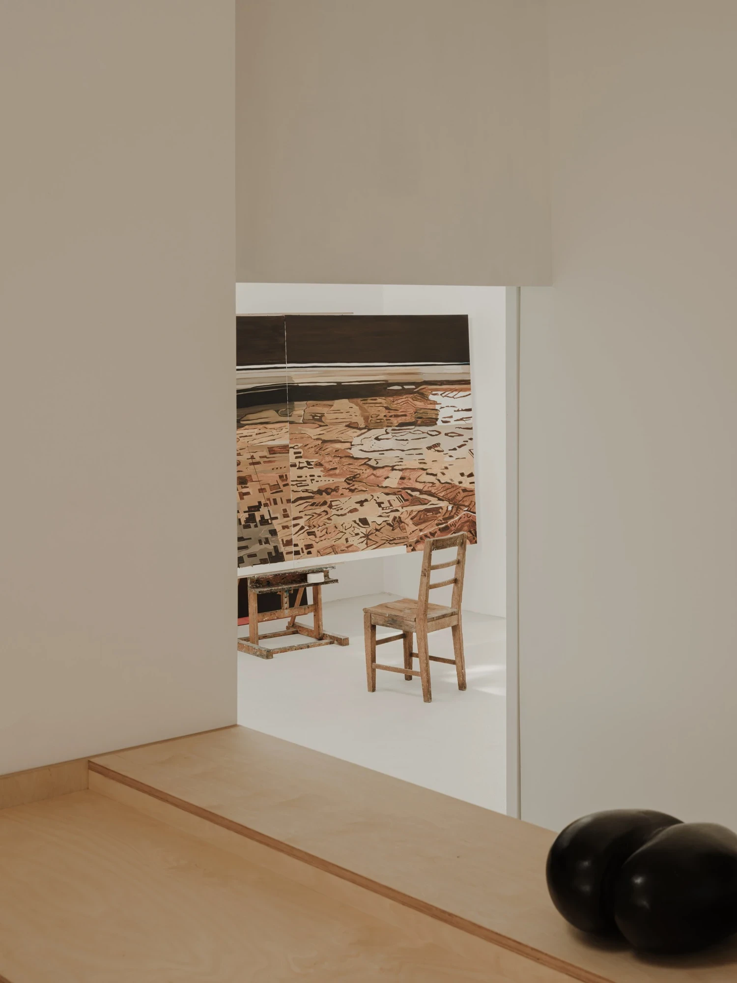 Moss by Pasparakis Friel, photographed by Peter Molloy — an oiled plywood bench and a wall opening reveal a painting studio with a spattered easel and worn timber chair.