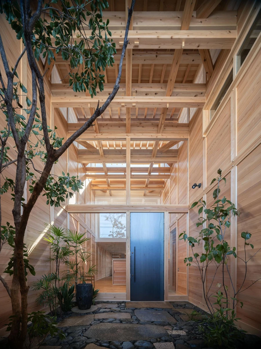 Single Family House in Aichi by Ryota Sekiya, photographed by Shun Fukuda — a blue-lit entrance void at dusk, framed by pale cedar boards with a young tree rising through the open sky-cut above.