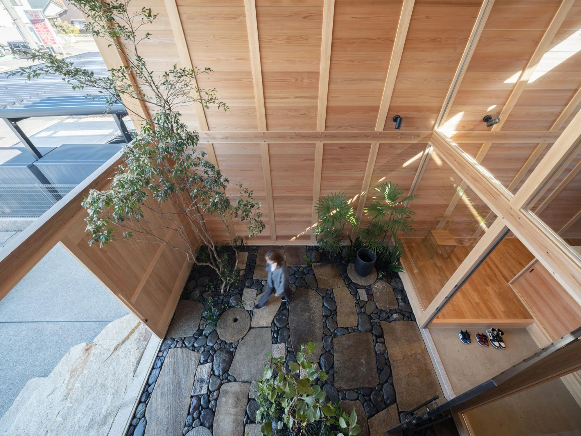 Single Family House in Aichi by Ryota Sekiya, photographed by Shun Fukuda — an overhead view down into a planted courtyard of stone paving and gravel, cedar beams framing the open sky above.
