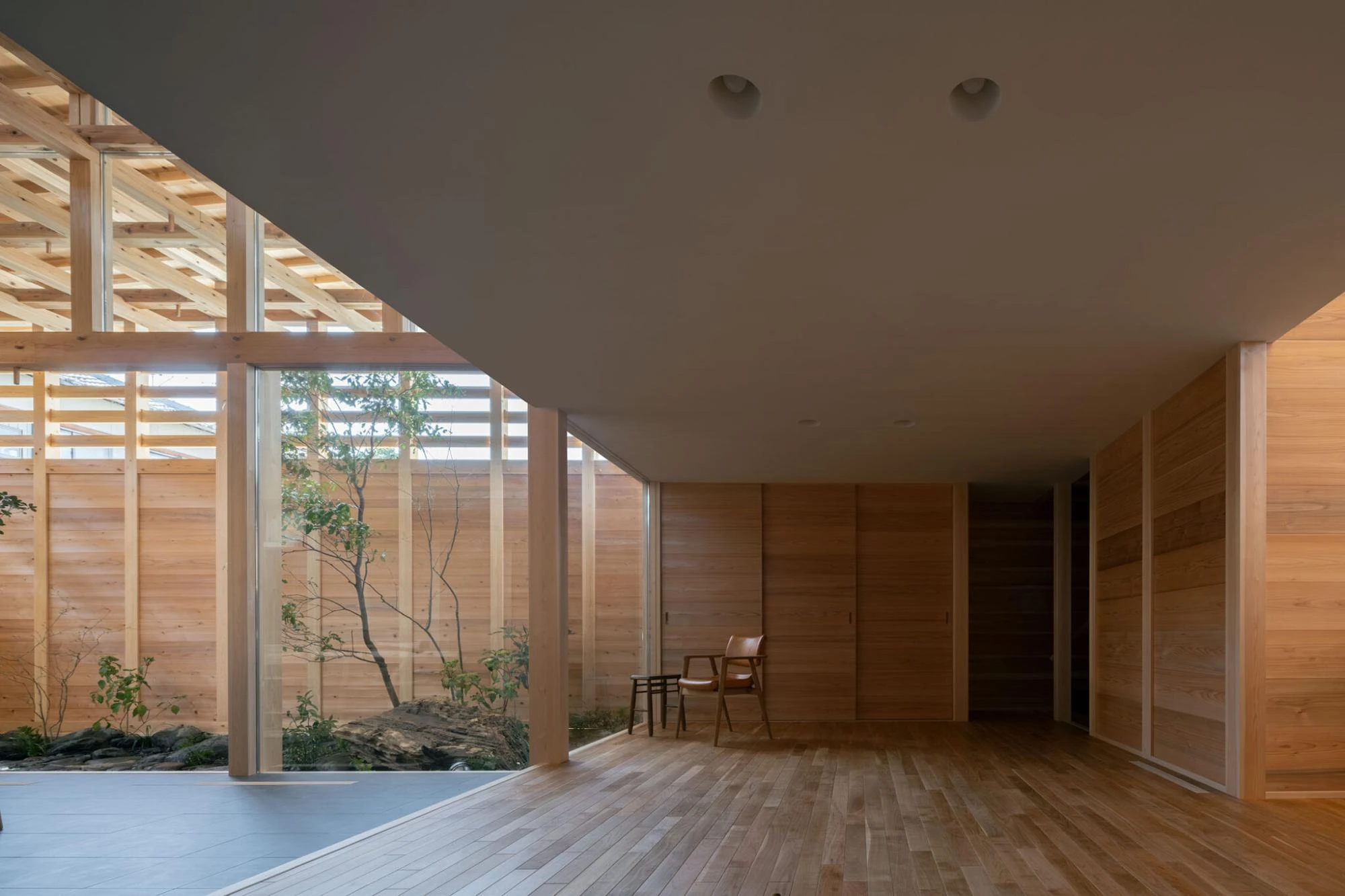 Single Family House in Aichi by Ryota Sekiya, photographed by Shun Fukuda — the low living room under a solid ceiling opens to a courtyard, a single leather chair set on pale oak flooring.