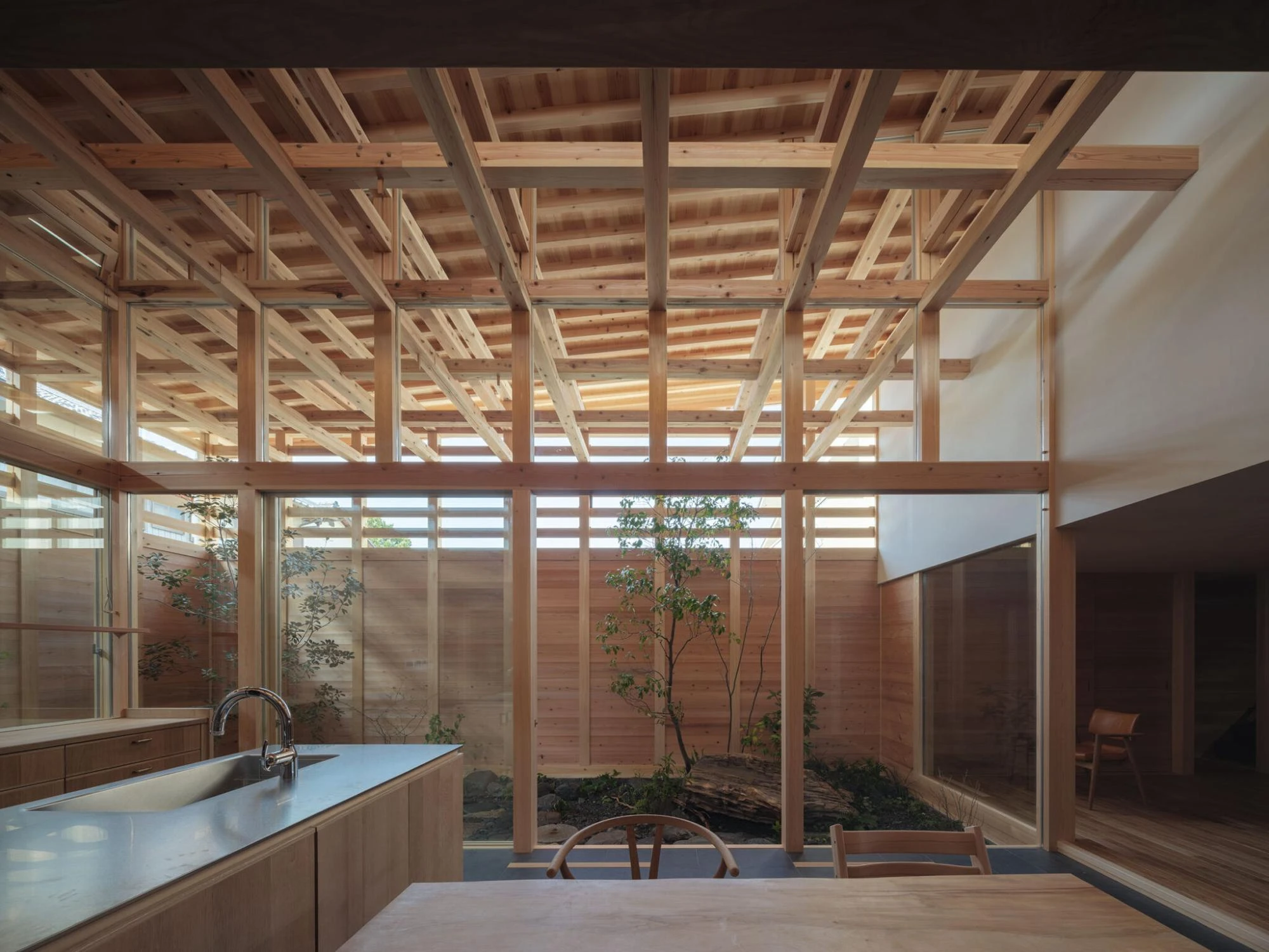 Single Family House in Aichi by Ryota Sekiya, photographed by Shun Fukuda — a stainless kitchen counter set beneath the tall beam lattice, the woven cedar grid rising to high-side skylight openings.