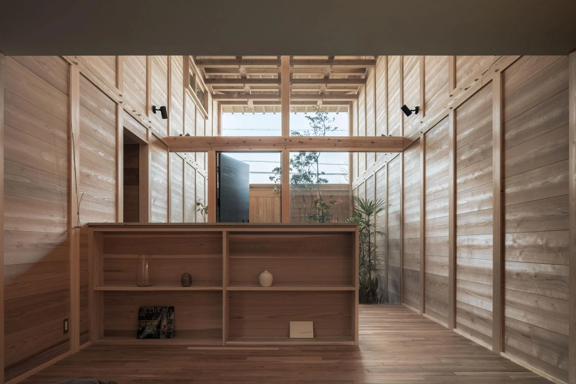Single Family House in Aichi by Ryota Sekiya, photographed by Shun Fukuda — a cedar-lined room with a low open shelving unit, a skylit window above framing a tree in the courtyard beyond.