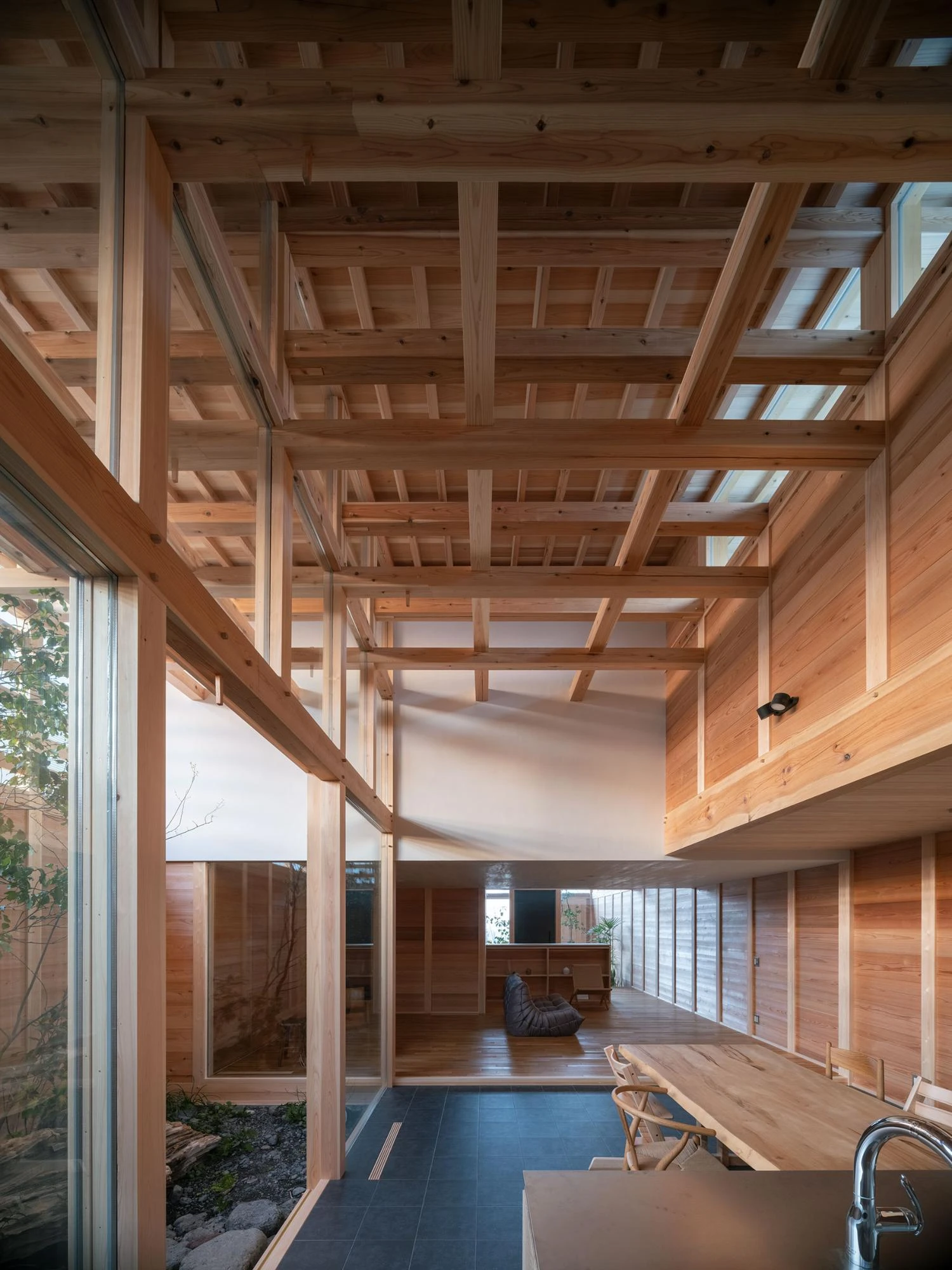 Single Family House in Aichi by Ryota Sekiya, photographed by Shun Fukuda — the tall lattice ceiling rises over a slate-tiled kitchen, distant living area glimpsed under a lower solid ceiling.