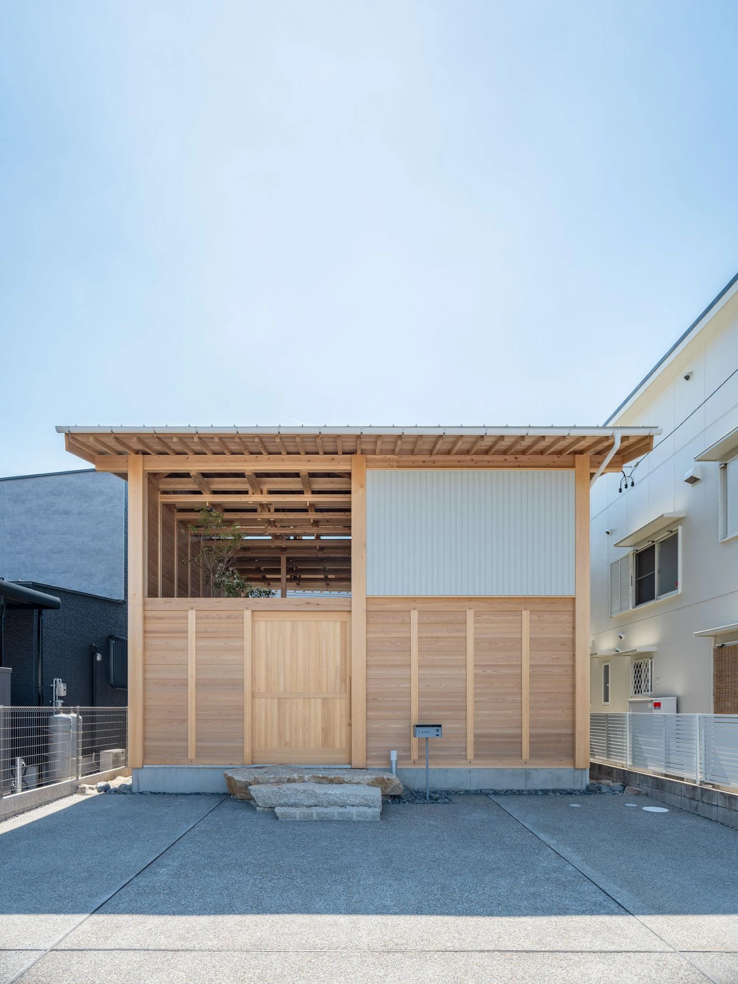Single Family House in Aichi by Ryota Sekiya, photographed by Shun Fukuda — the street facade, a cedar-clad box with an open framed void at upper left, set on concrete paving under a clear sky.